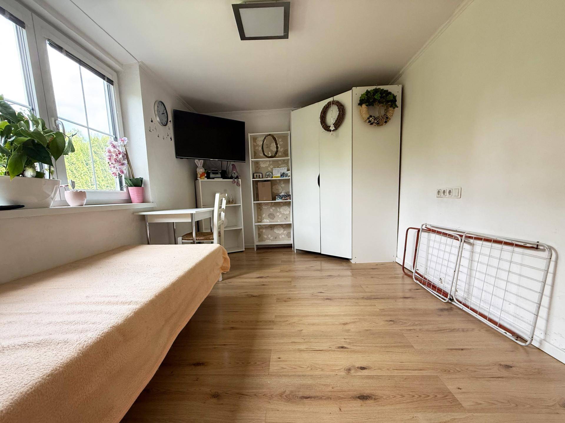Helles Zimmer mit Holzboden, Einzelbett, Schrank und großem Fenster mit Blick ins Grüne.