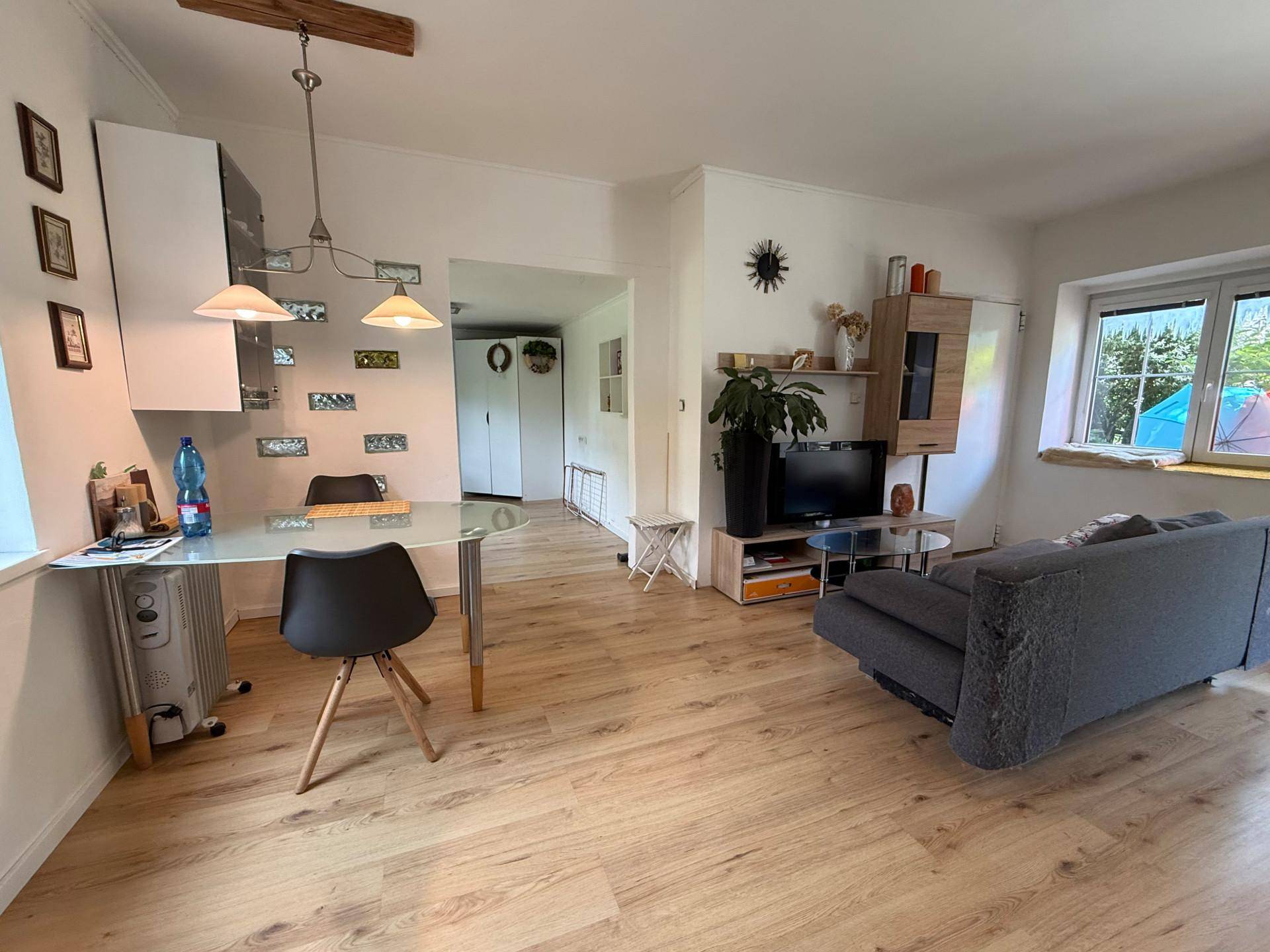 Offener Wohn- und Essbereich mit Holzboden, Esstisch und Sofa im Hintergrund.