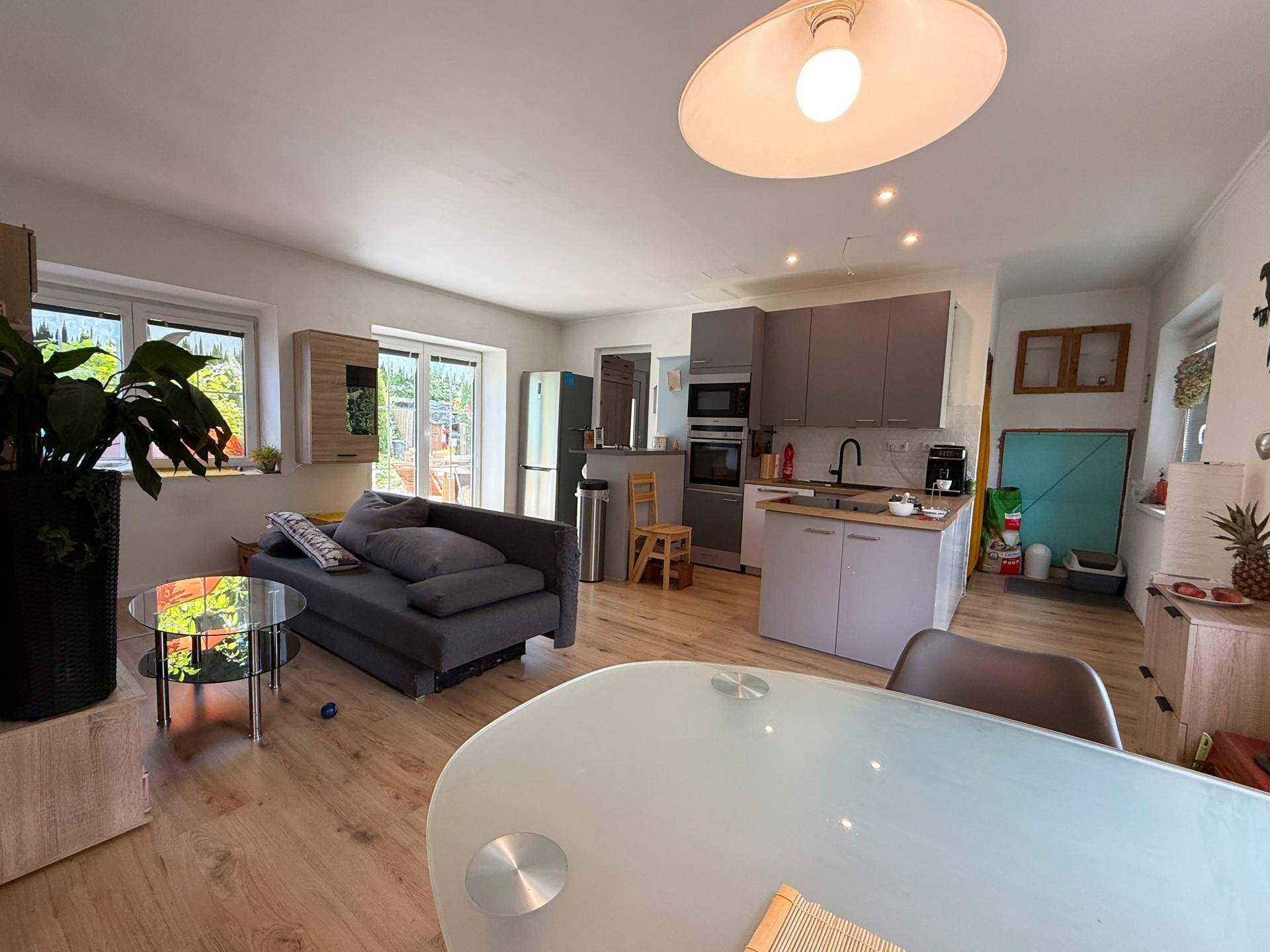 Geräumiger offener Wohnbereich mit Holzboden, Sofa und integrierter Küche in modernen Farben.