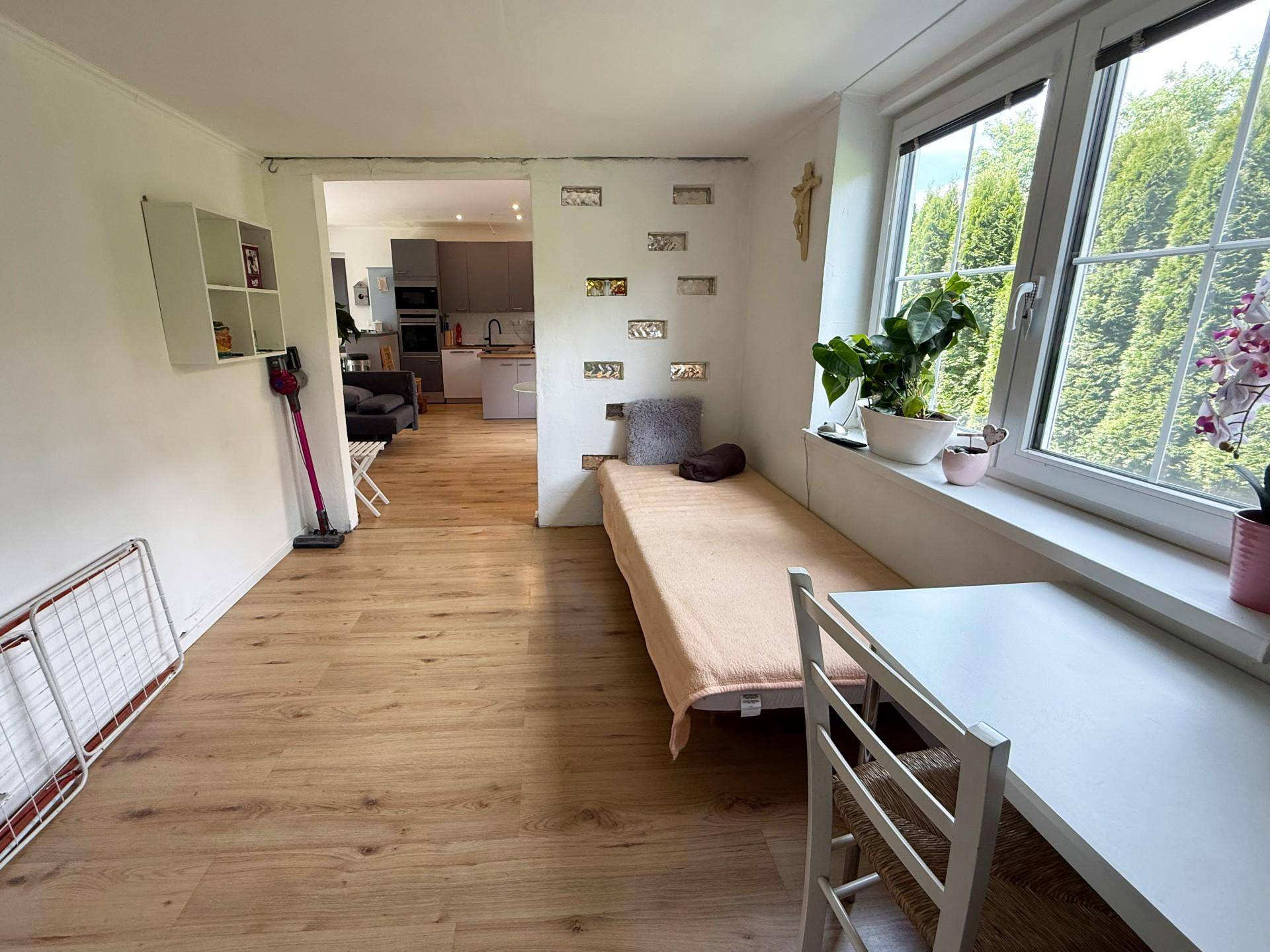 Helles Zimmer mit Holzboden, Einzelbett und großem Fenster mit Blick auf die Bäume.
