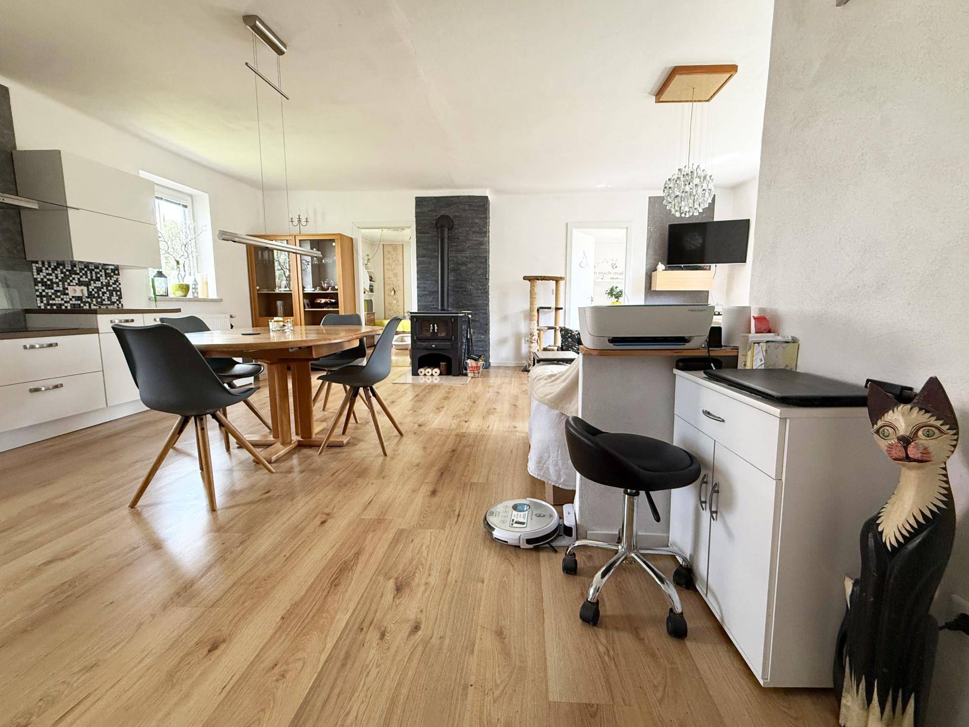 Offener Wohn-Essbereich mit Holzboden, Esstisch und Kaminofen im Hintergrund.