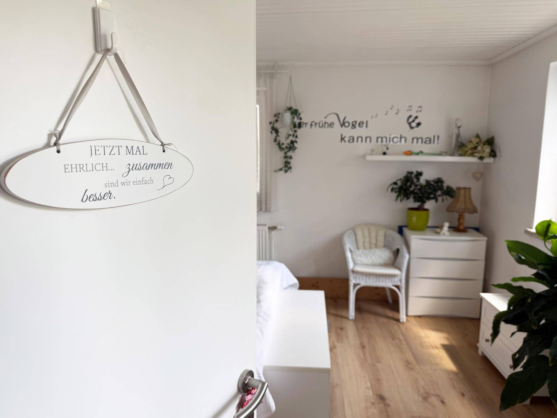 Wanddekoration mit Schriftzug in einem hellen Innenraum mit Holzboden.