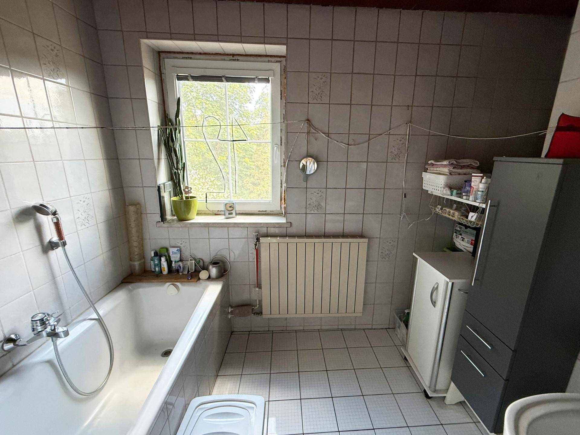 Gefliestes Badezimmer mit Badewanne, Fenster und Heizkörper.