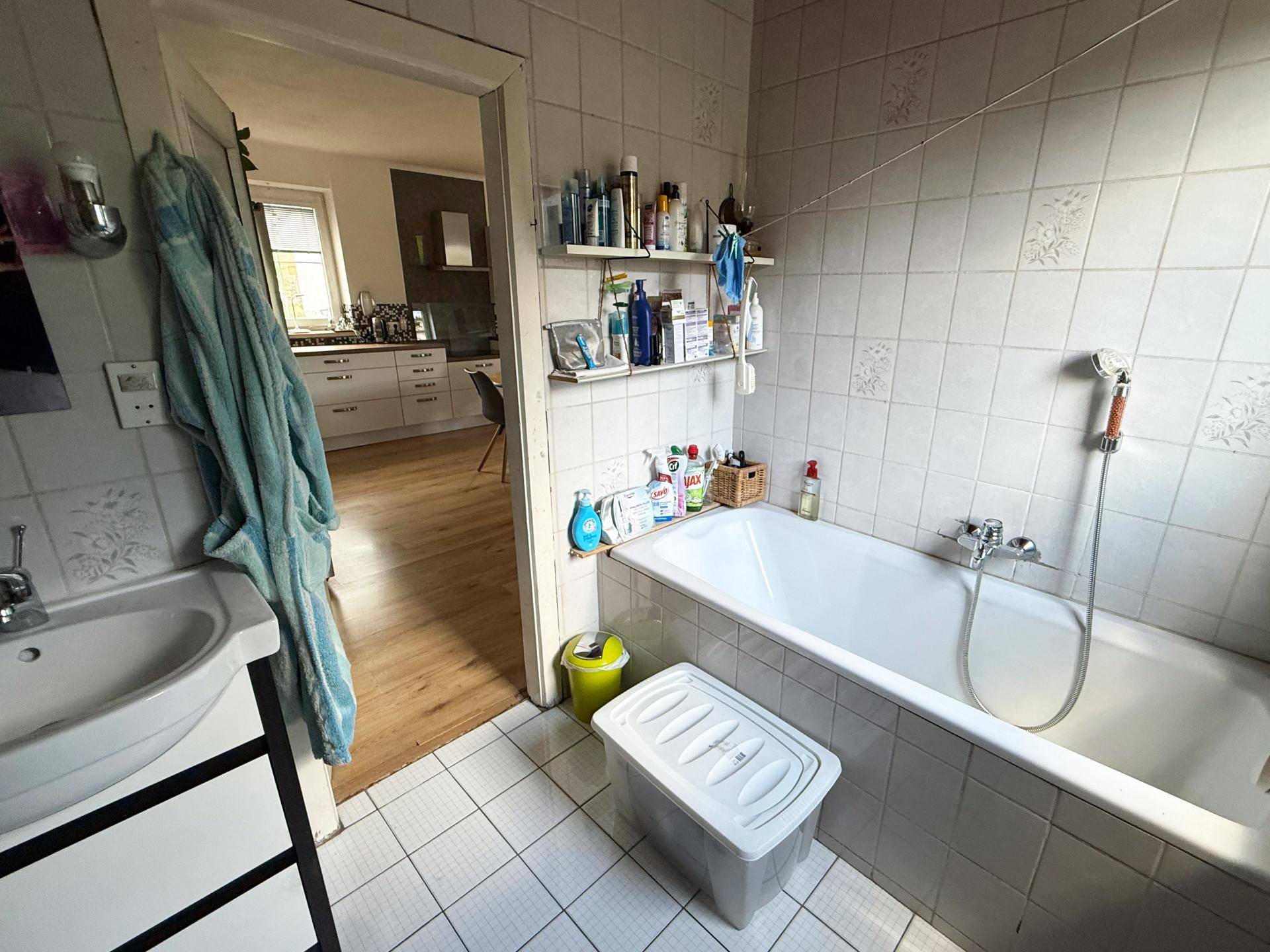 Badezimmer mit Badewanne, Waschbecken und Blick in den angrenzenden Raum.