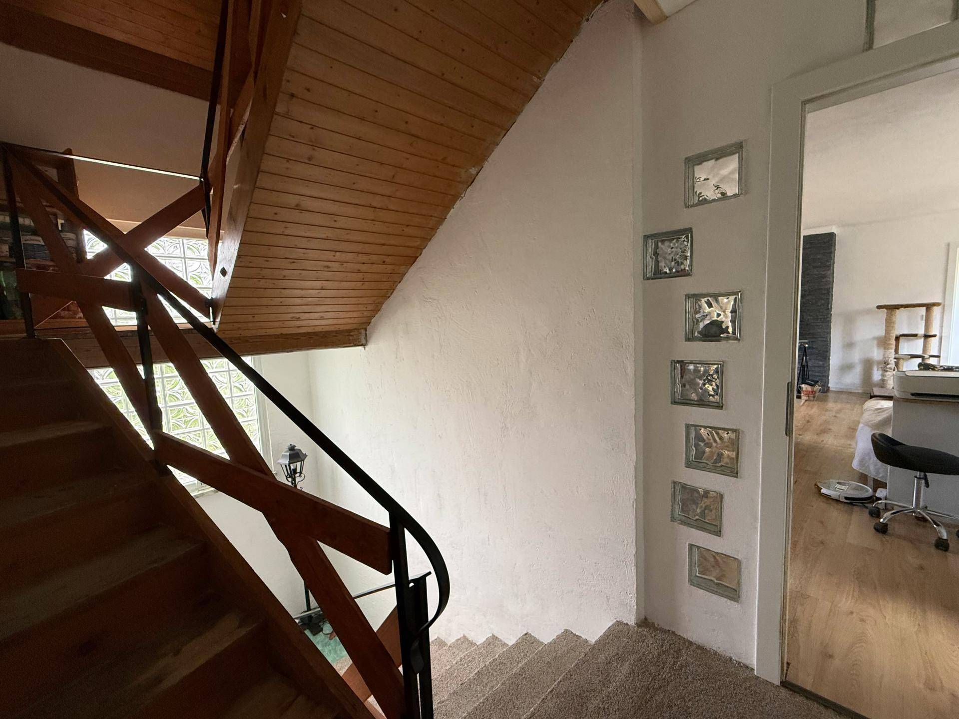 Holztreppe mit Teppichstufen und Geländer, die in das obere Stockwerk führt.