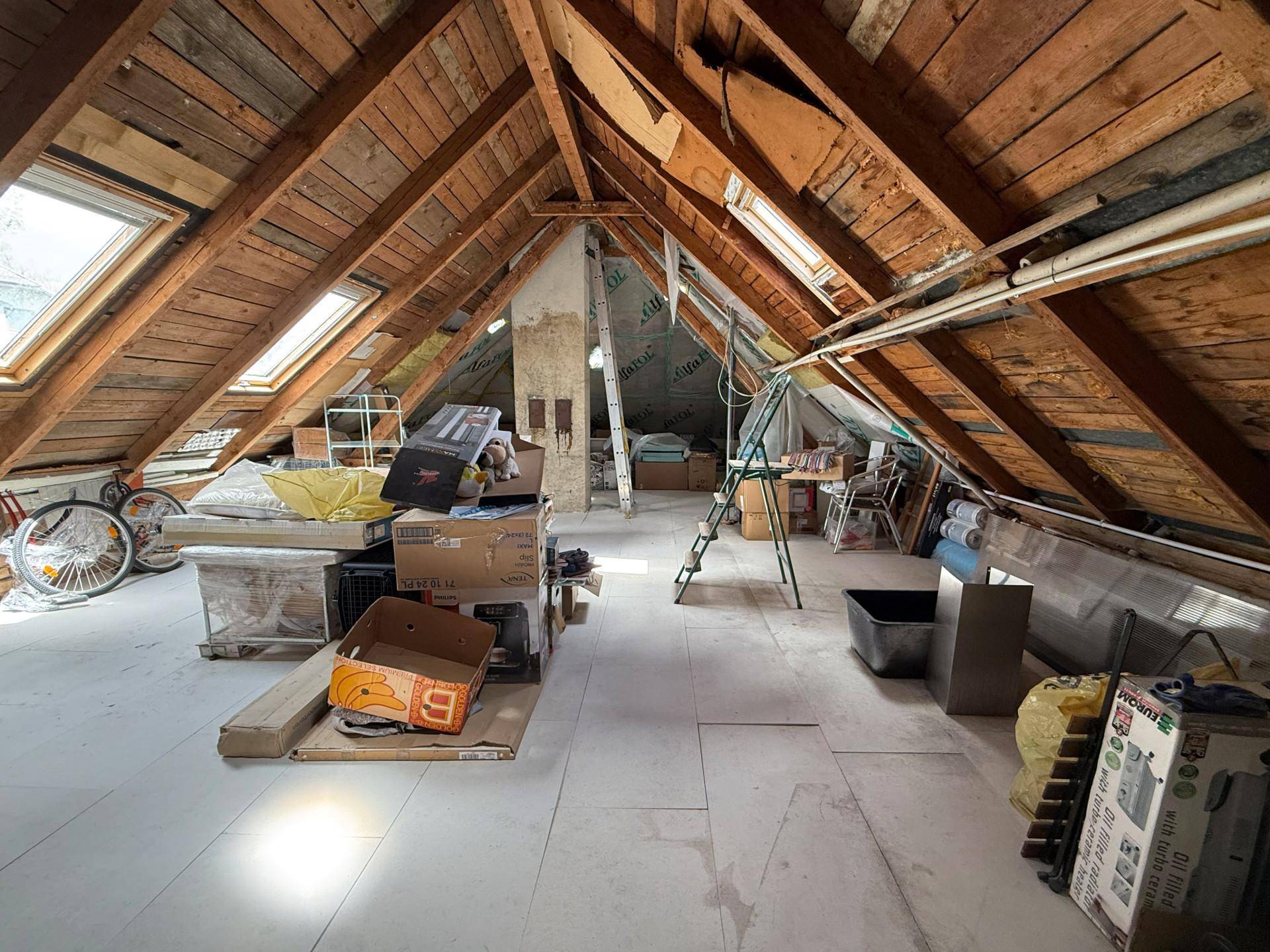Geräumiger Dachboden mit sichtbaren Holzbalken, Dachfenstern und Stauraum.