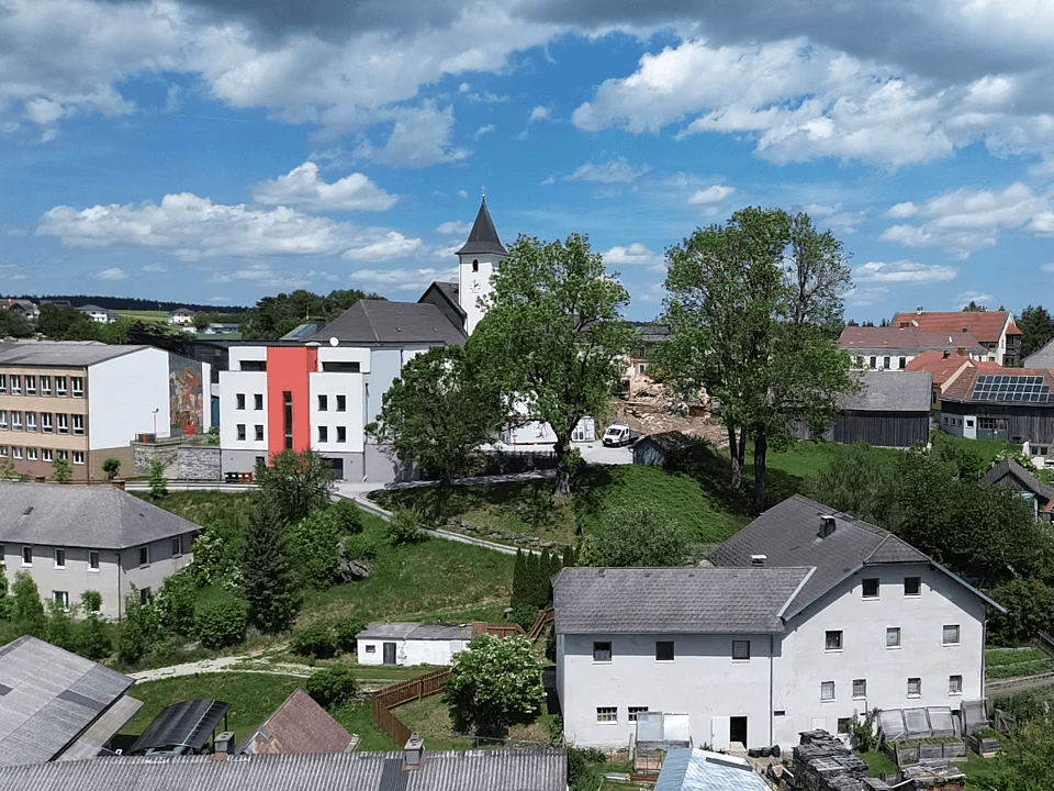 Panoramablick auf das Dorfzentrum mit Kirche, Wohngebäuden und grünen Hügeln.