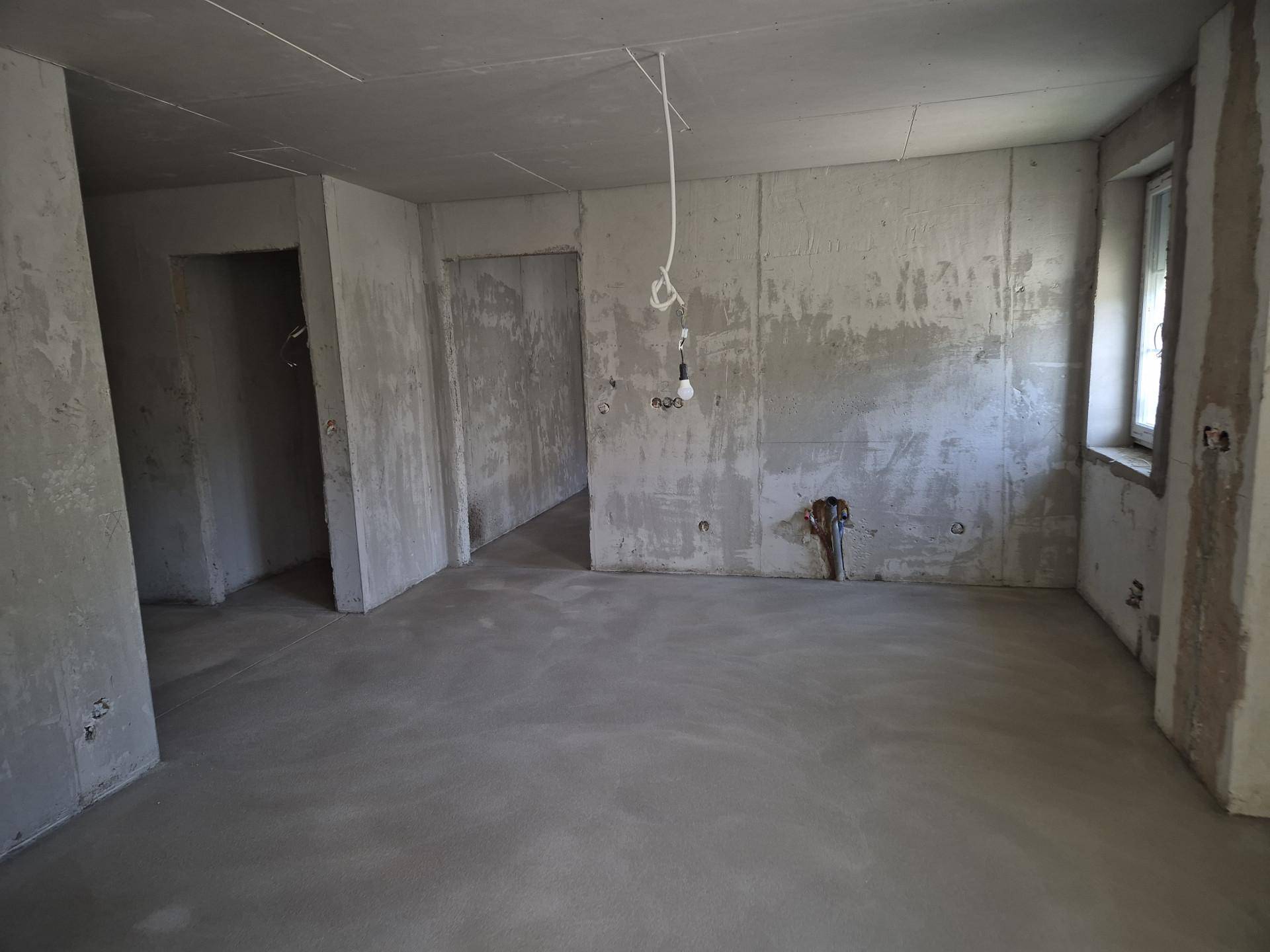Rohbauzimmer mit Betonwänden und -boden, vorbereitet für den weiteren Innenausbau.