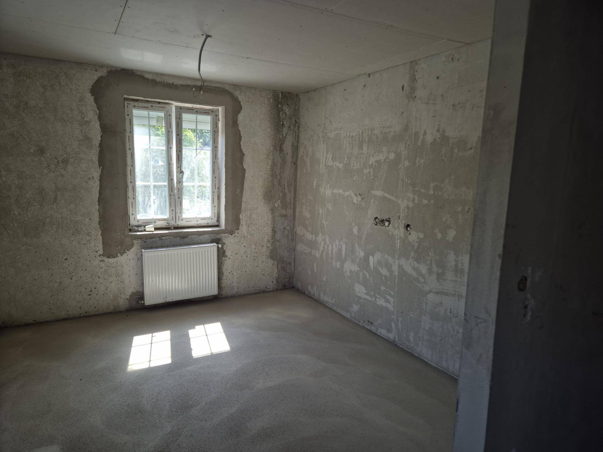 Unfertiger Raum mit Betonwänden, Fenster und Heizkörper, wartet auf den Innenausbau.