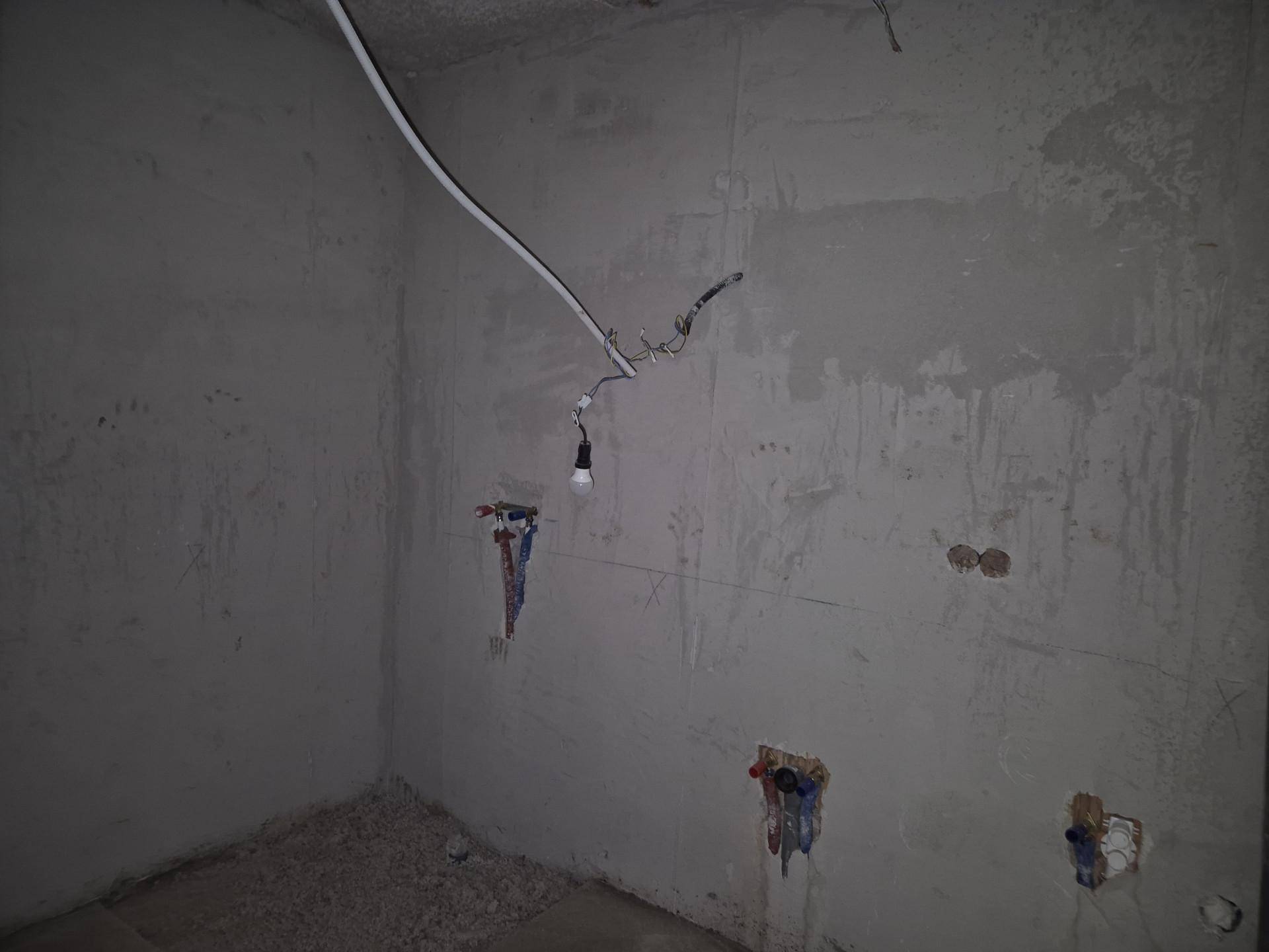 Rohbauzimmer mit sichtbaren Leitungen und Betonwänden, bereit für die Installationen.