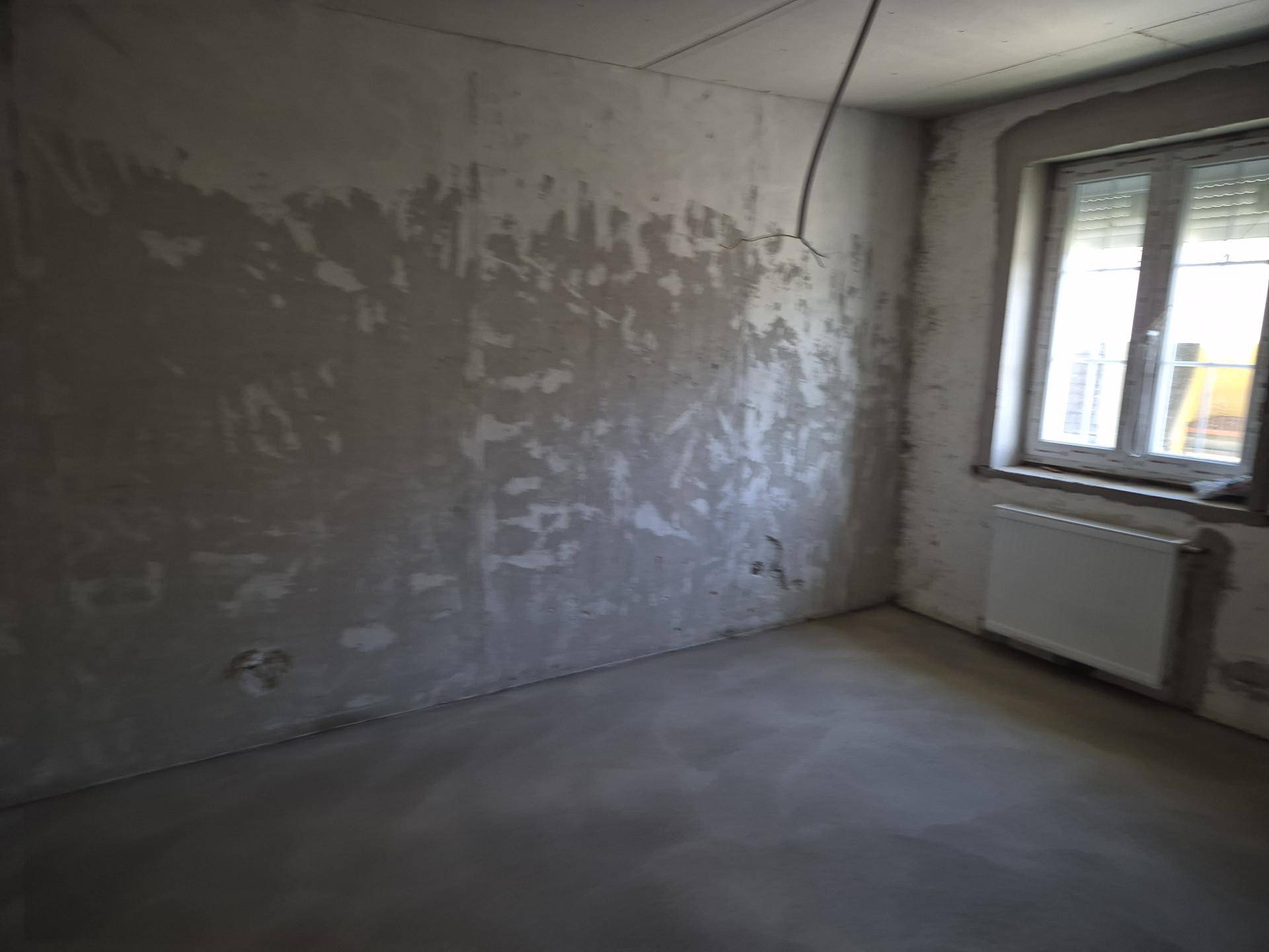 Unfertiger Raum mit Betonwänden, Fenster und Heizkörper, wartet auf den Innenausbau.