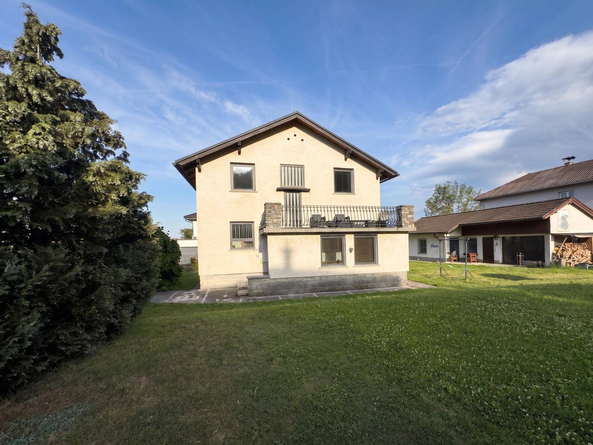 Rückansicht des Hauses mit Balkon und weitläufigem Gartenbereich bei Sonnenschein.