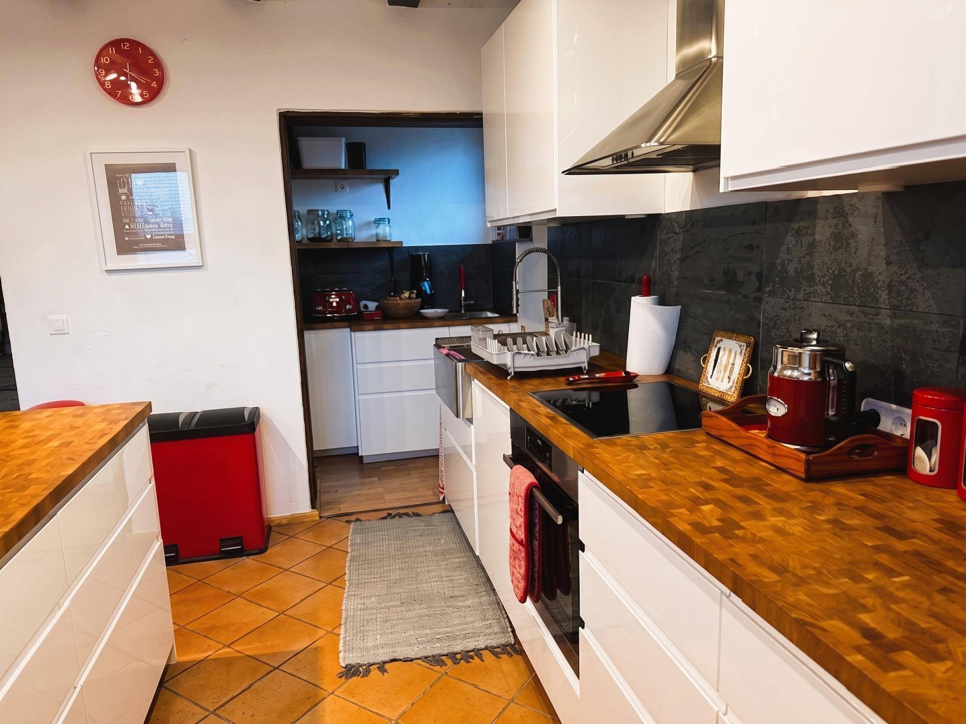 Moderne Küche mit weißen Schränken, Holz-Arbeitsplatten und Terrakotta-Bodenfliesen.