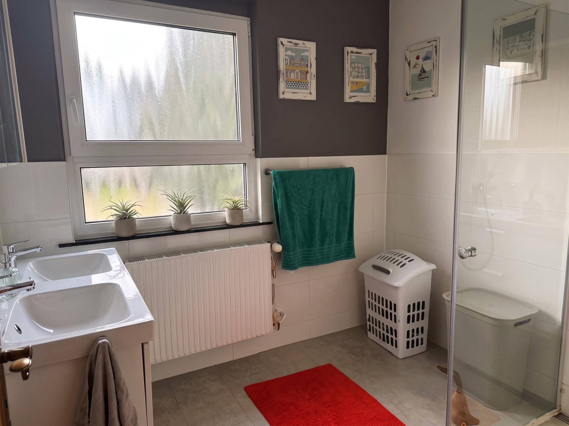 Helles Badezimmer mit Doppelwaschbecken, großer Dusche und Fenster für Tageslicht.