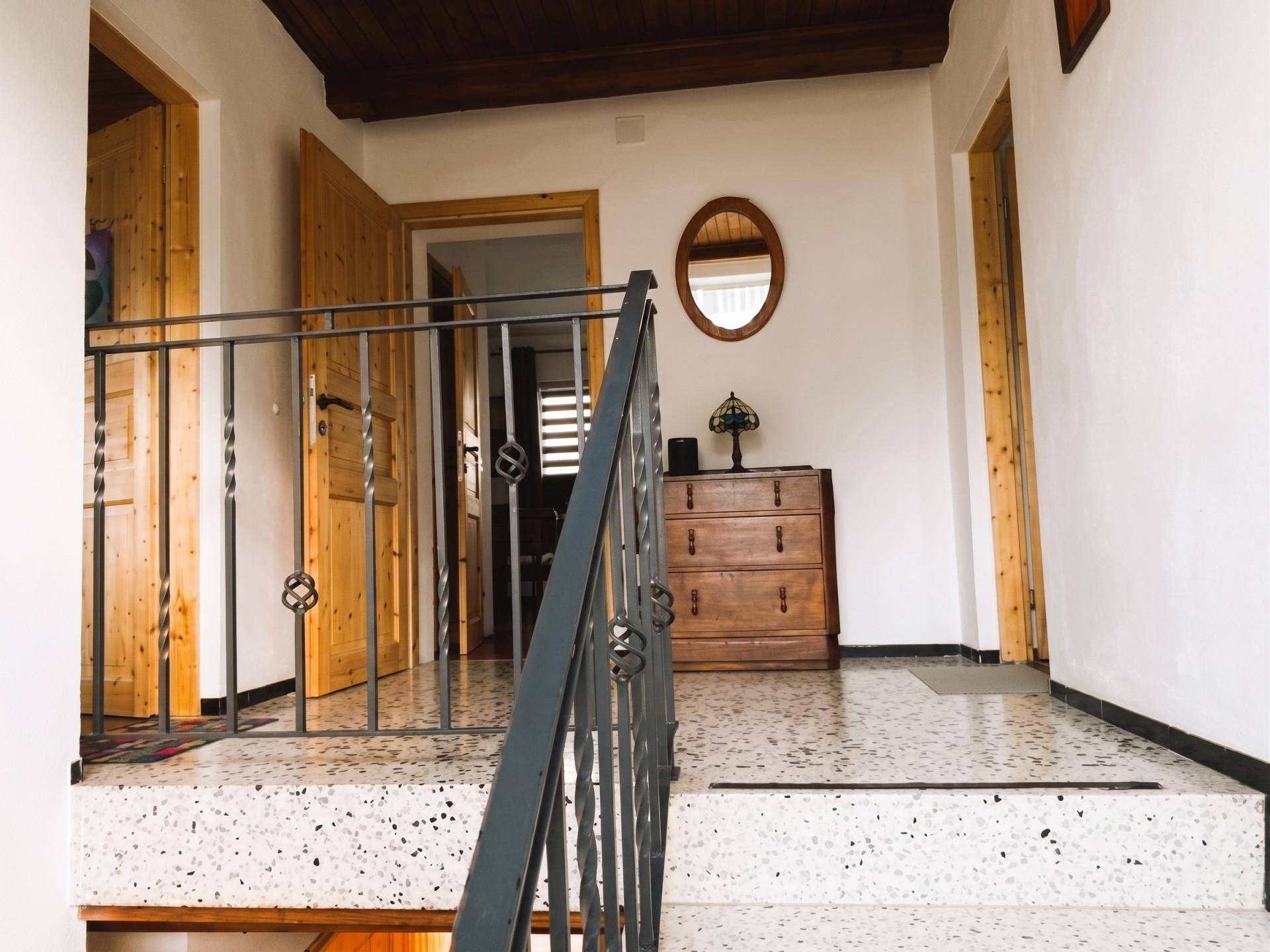 Geräumiger Flur mit Terrazzoboden, Holzdecke und Treppengeländer aus Metall.
