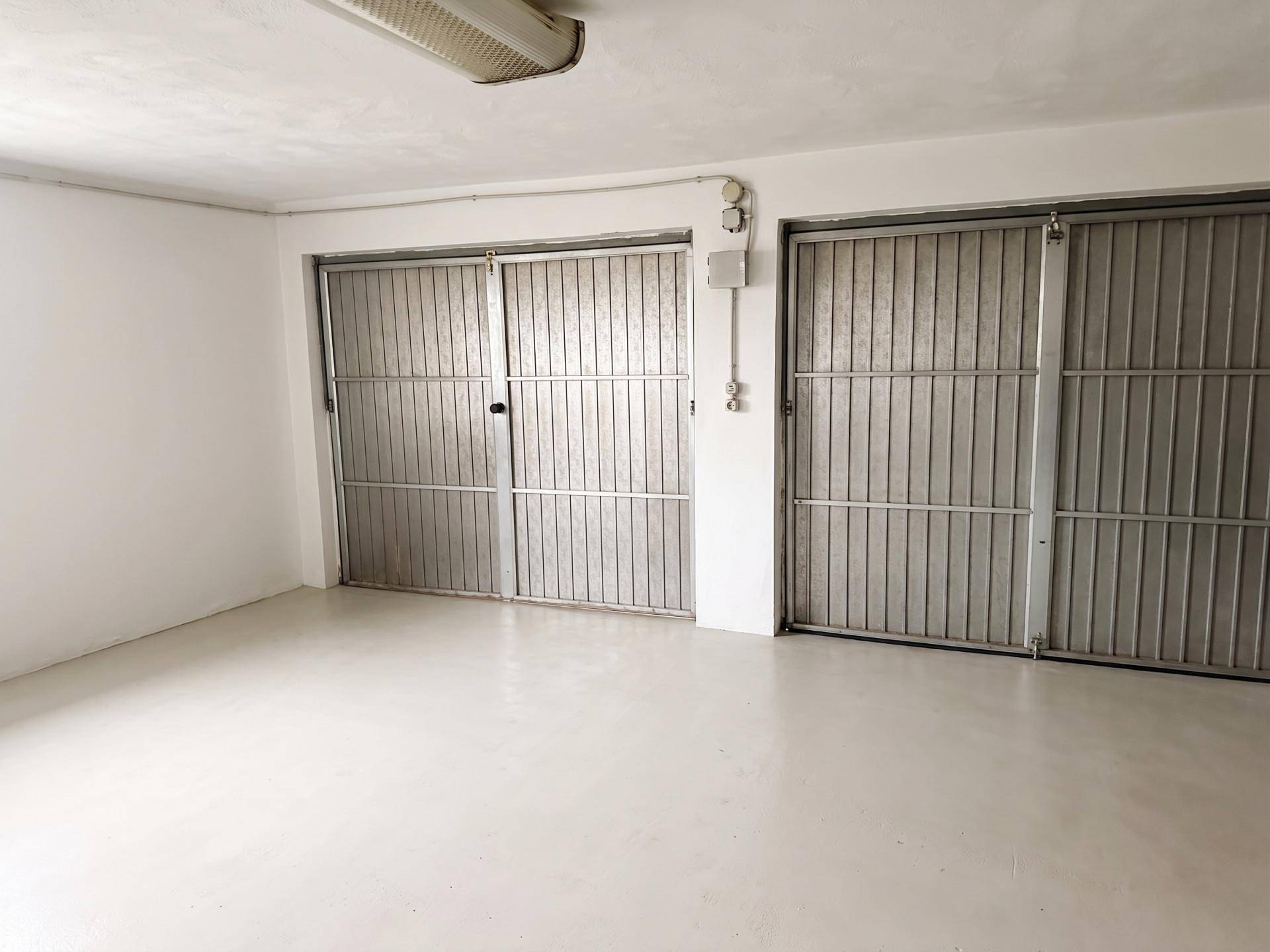 Geräumige Garage mit zwei Metalltoren und hellem Betonboden, gut beleuchtet.