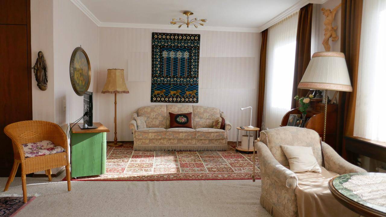 Gemütliches Wohnzimmer mit traditionellen Möbeln, Teppichen und viel Tageslicht durch das Fenster.