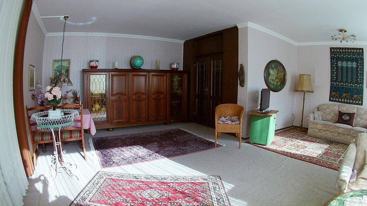 Geräumiger Wohn- und Essbereich mit traditionellen Holzmöbeln, Teppichen und viel Tageslicht.