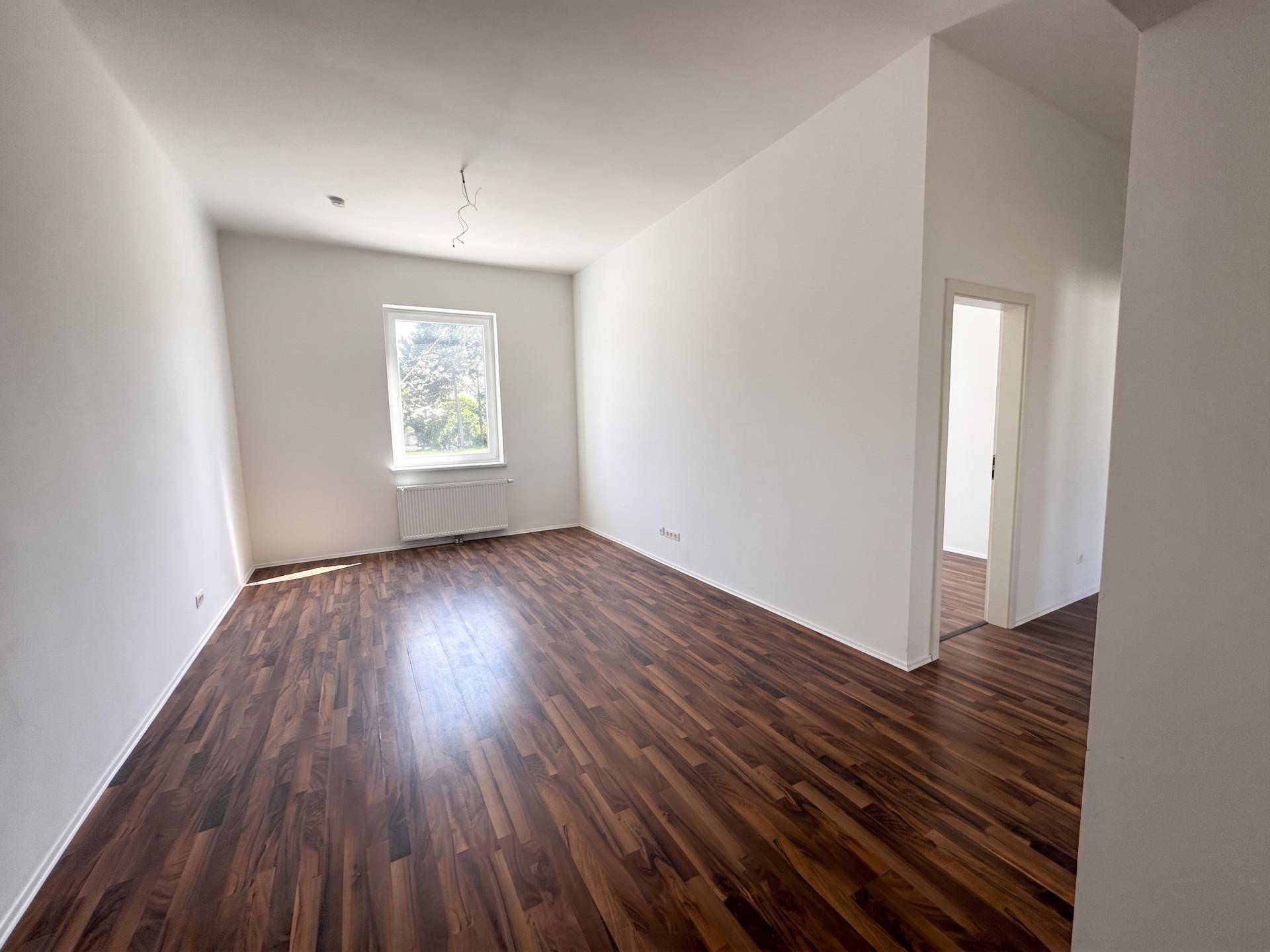 Leeres Schlafzimmer mit dunklem Laminatboden, weißen Wänden und einem Fenster.