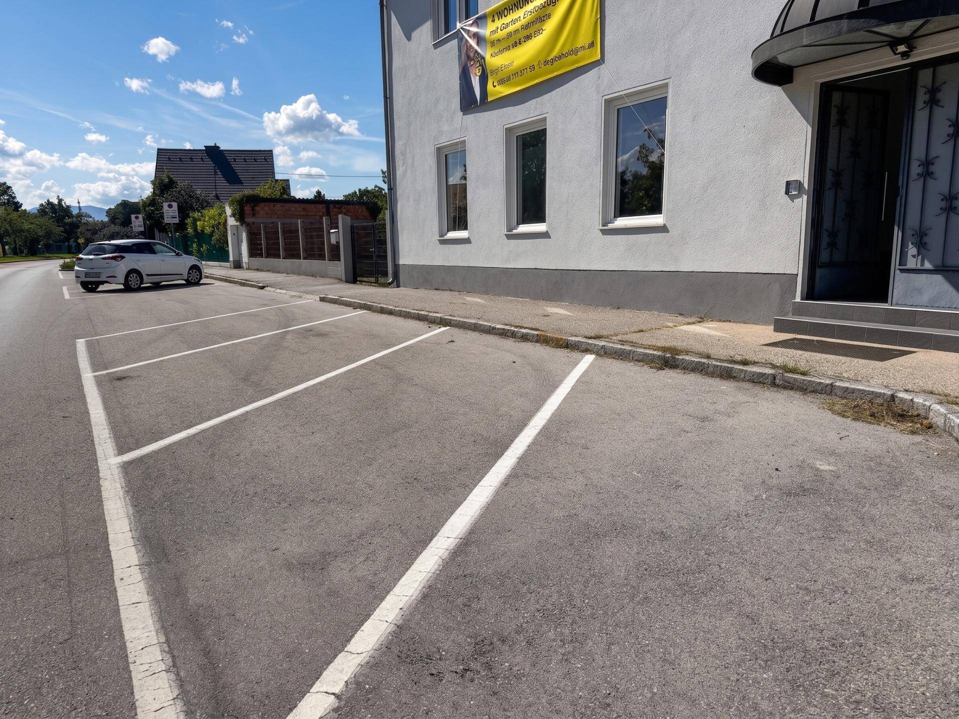 Außenbereich mit markierten Parkplätzen vor dem Eingang eines Wohngebäudes.