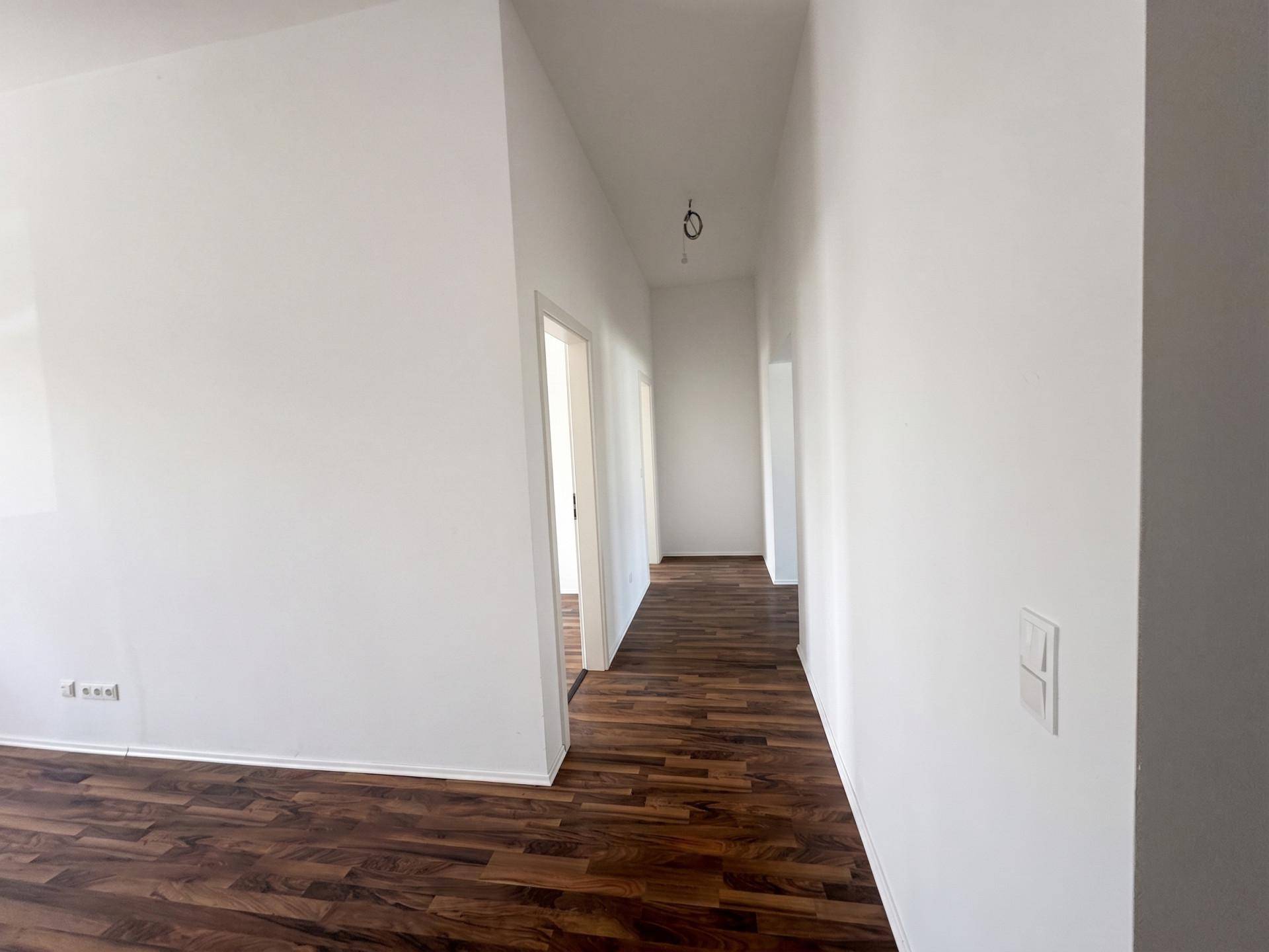 Heller Flur mit dunklem Laminatboden und weißen Wänden, der zu weiteren Räumen führt.
