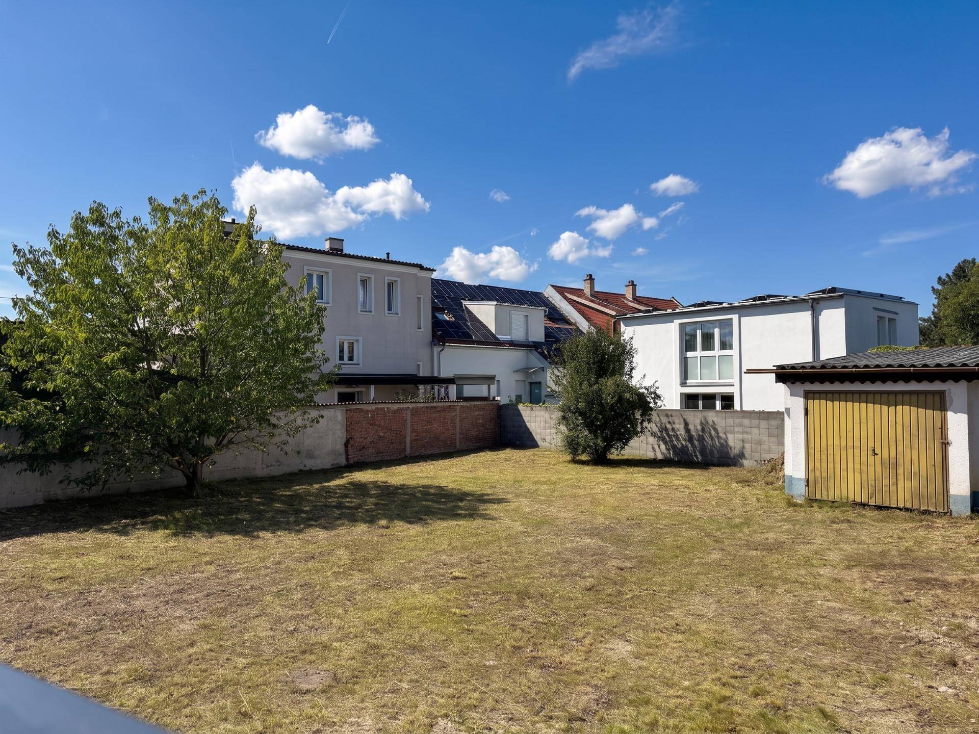 Großer Gartenbereich mit Rasen, Bäumen und Blick auf benachbarte Wohnhäuser.