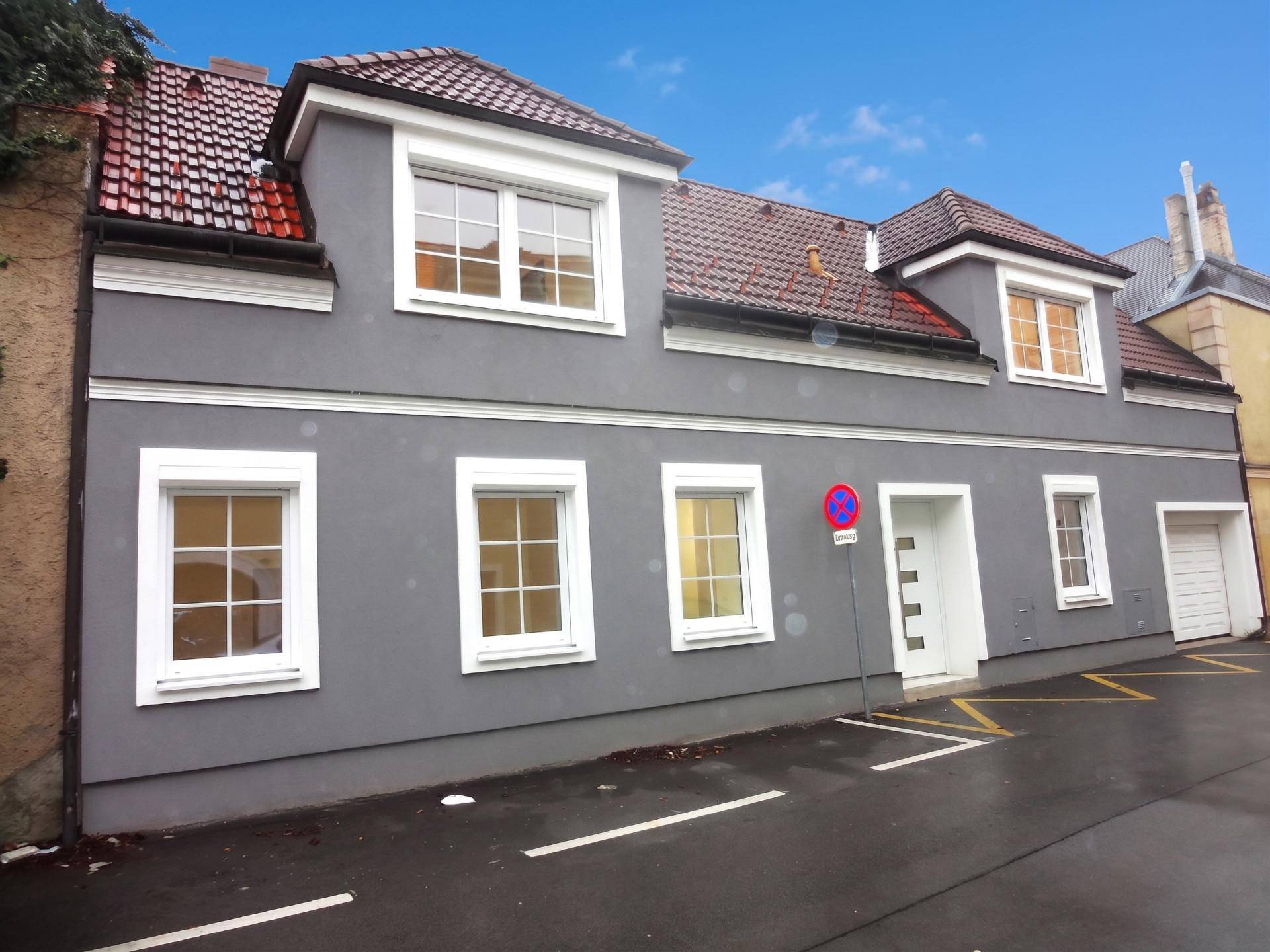Graue Hausfassade mit roten Ziegeldächern, weißen Fenstern und integrierter Garage.