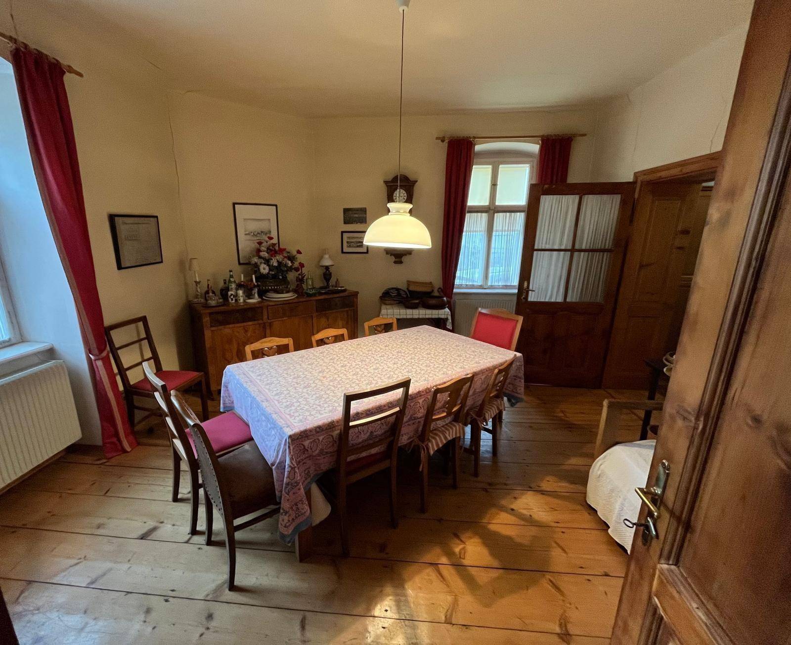 Traditionelles Esszimmer mit großem Holztisch, Holzboden und roten Vorhängen.
