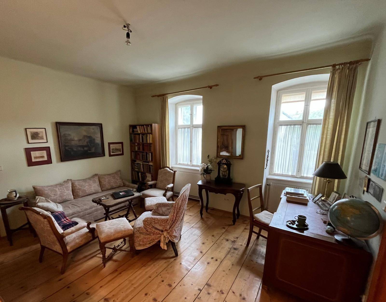 Gemütliches Wohnzimmer mit Holzboden, traditionellen Möbeln und großen Fenstern.