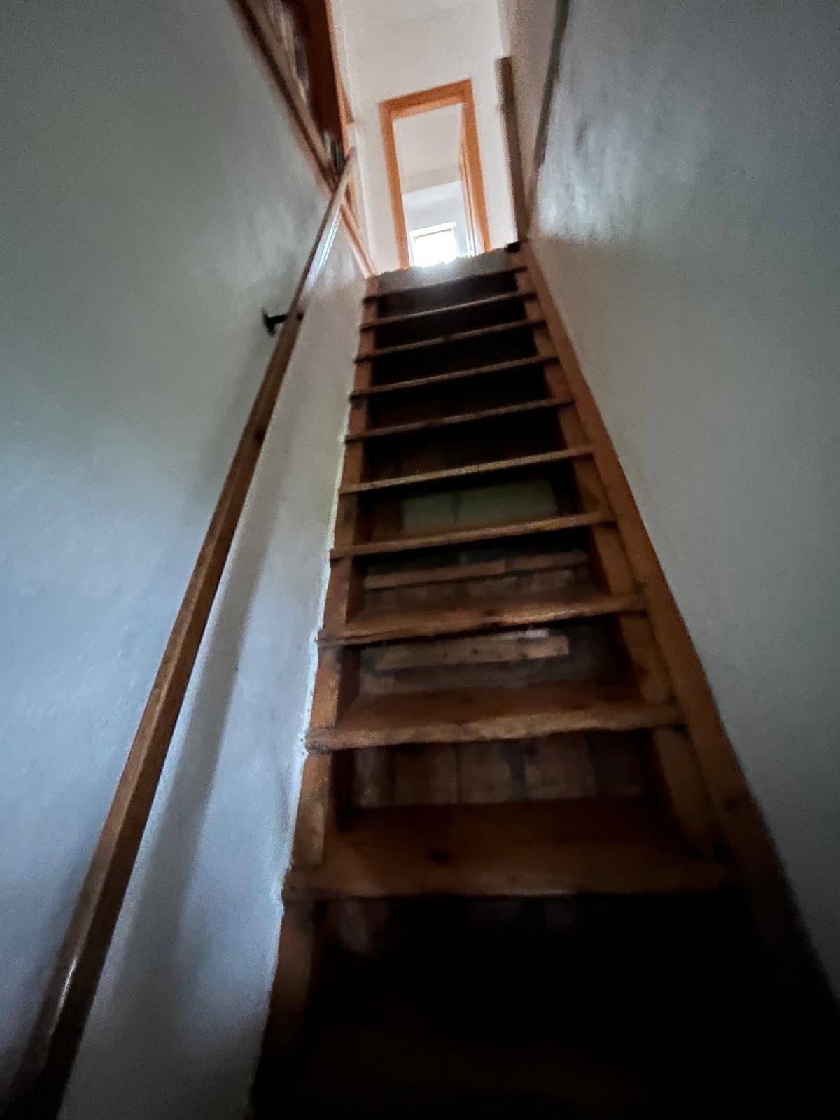 Schmale Holztreppe führt in ein oberes Stockwerk mit einfacher Gestaltung.