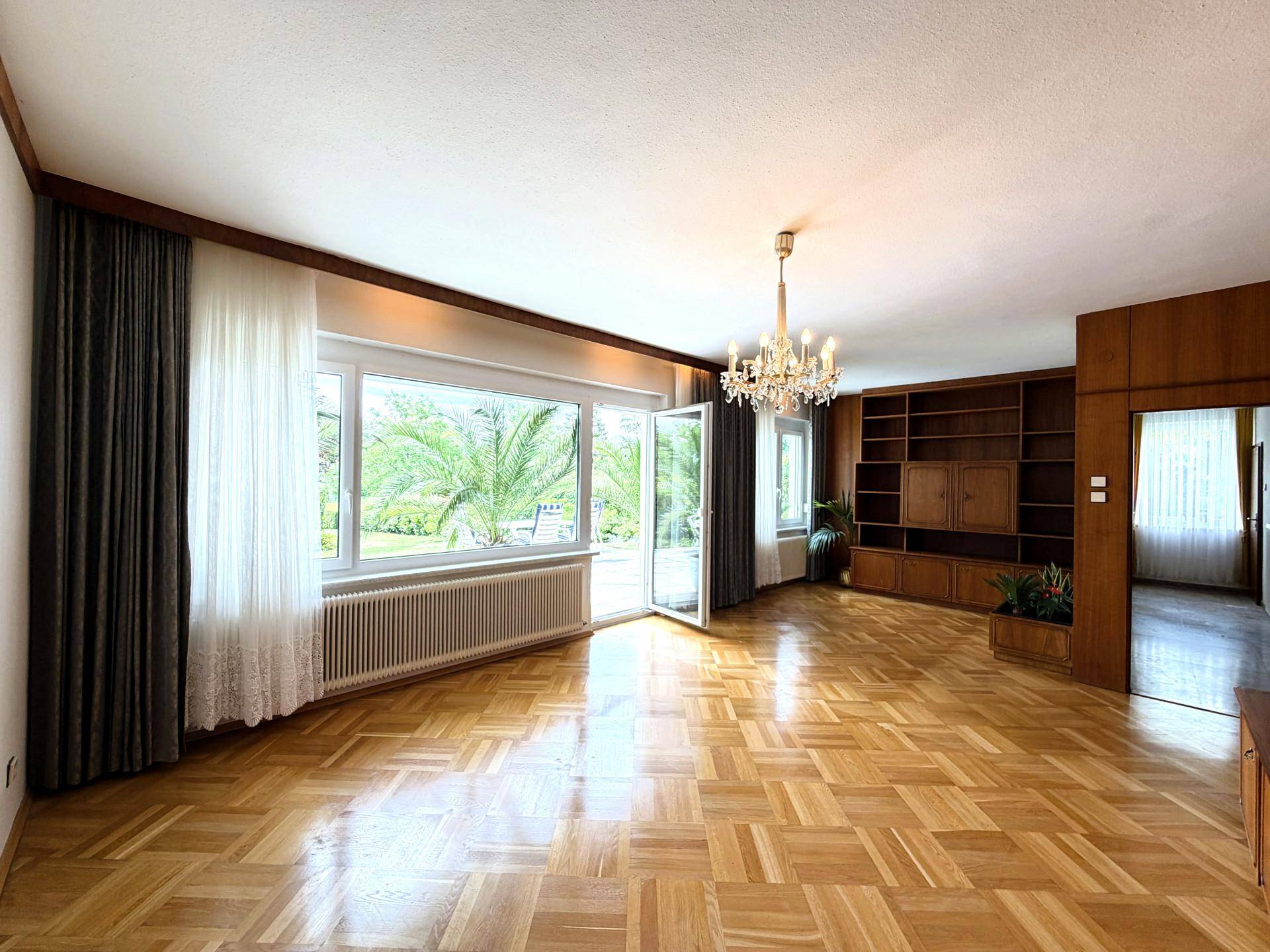 Geräumiges Wohnzimmer mit Holzeinbauten, Parkettboden und viel Tageslicht.