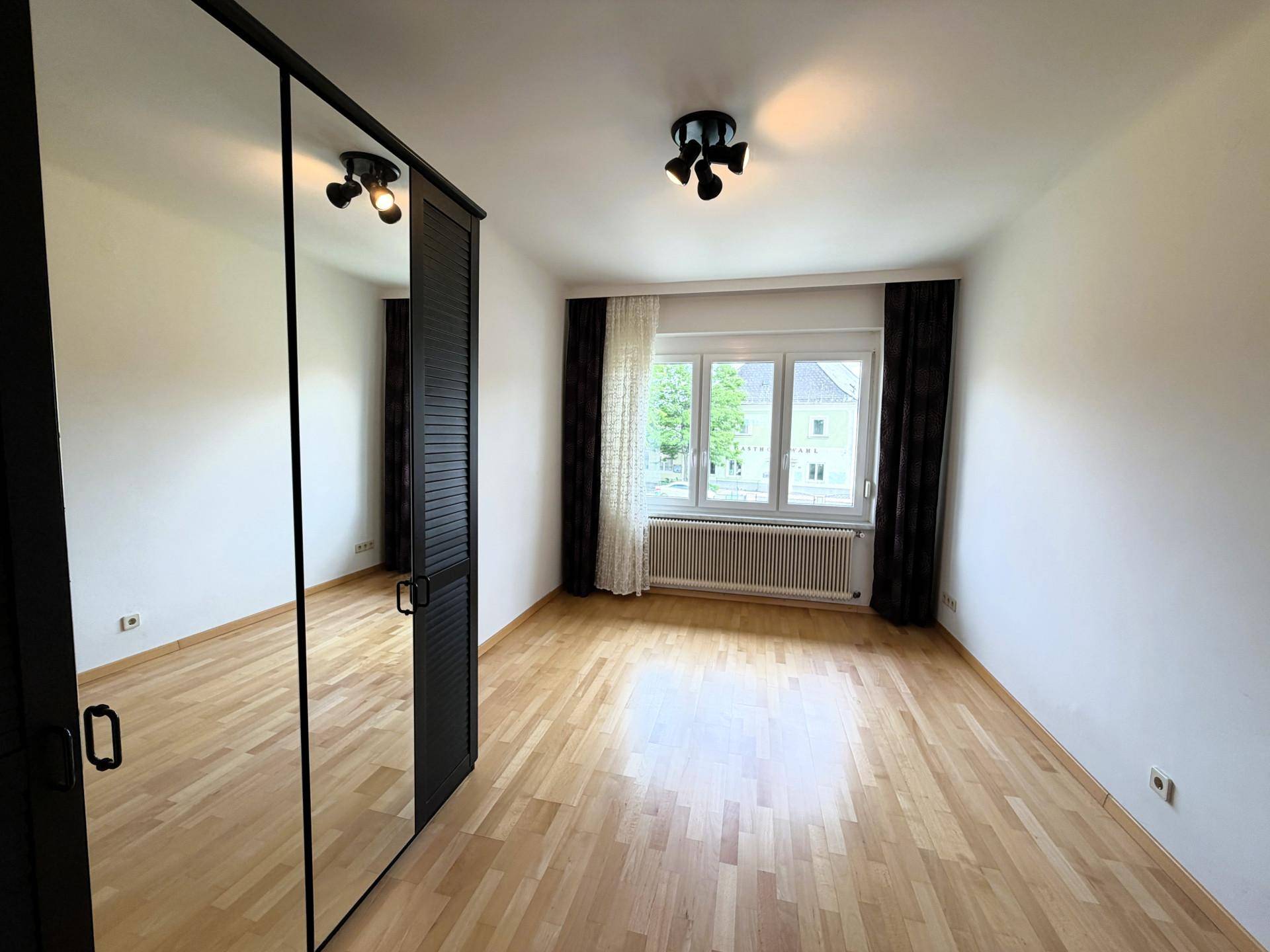 Geräumiges Schlafzimmer mit Parkettboden, Spiegelschrank und Fenster mit Blick nach draußen.