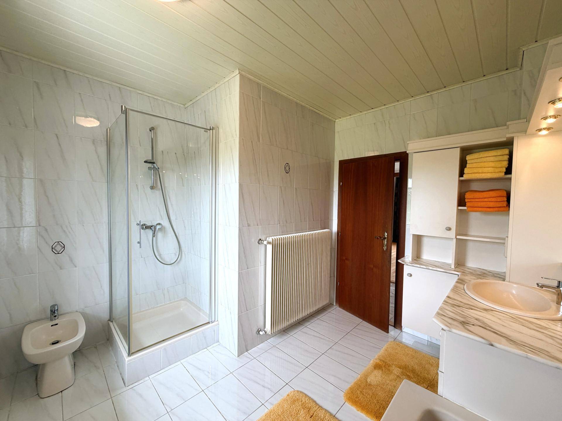Modernes Badezimmer mit Duschkabine, Bidet und Waschtisch, hell gefliest.