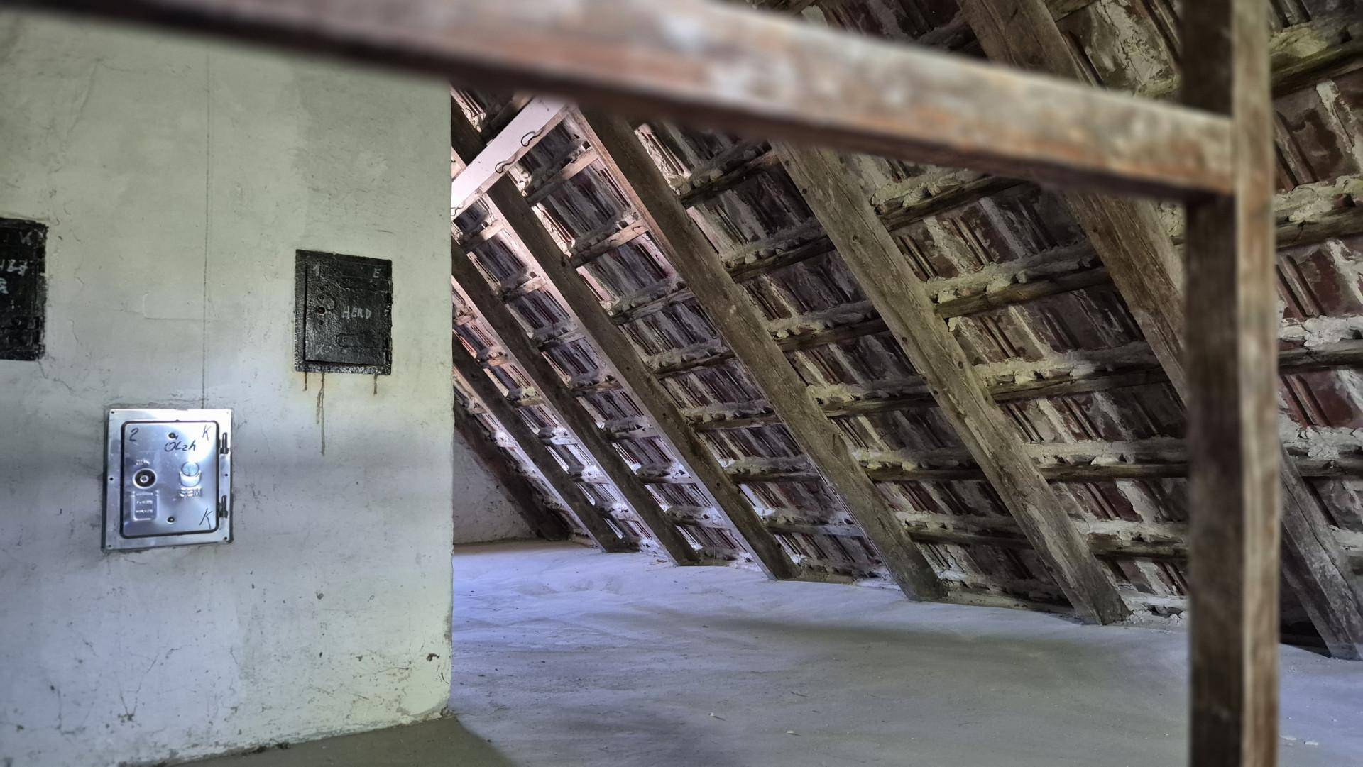 Unausgebauter Dachboden mit sichtbaren Holzbalken und Ziegeln, bietet Ausbaupotenzial.