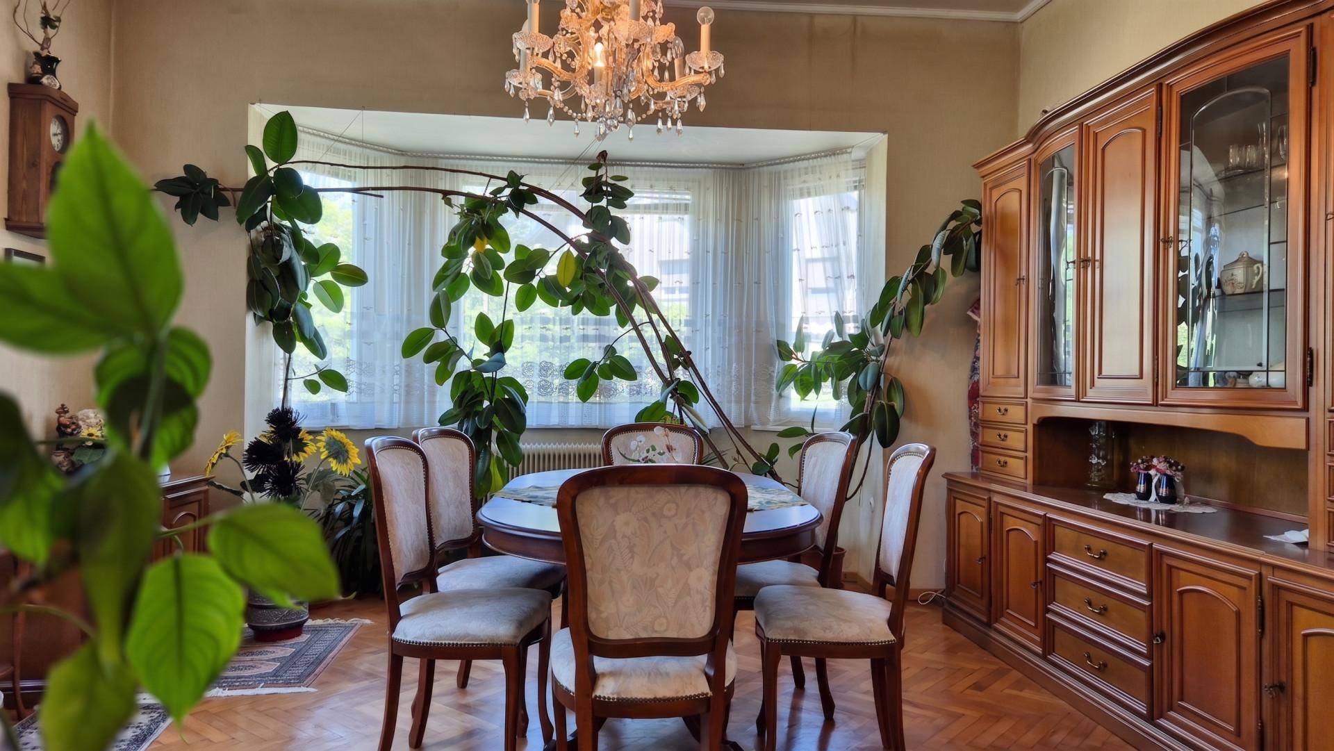 Traditioneller Essbereich mit Holztisch, Stühlen und einem großen Erkerfenster, geschmückt mit einem Kronleuchter.