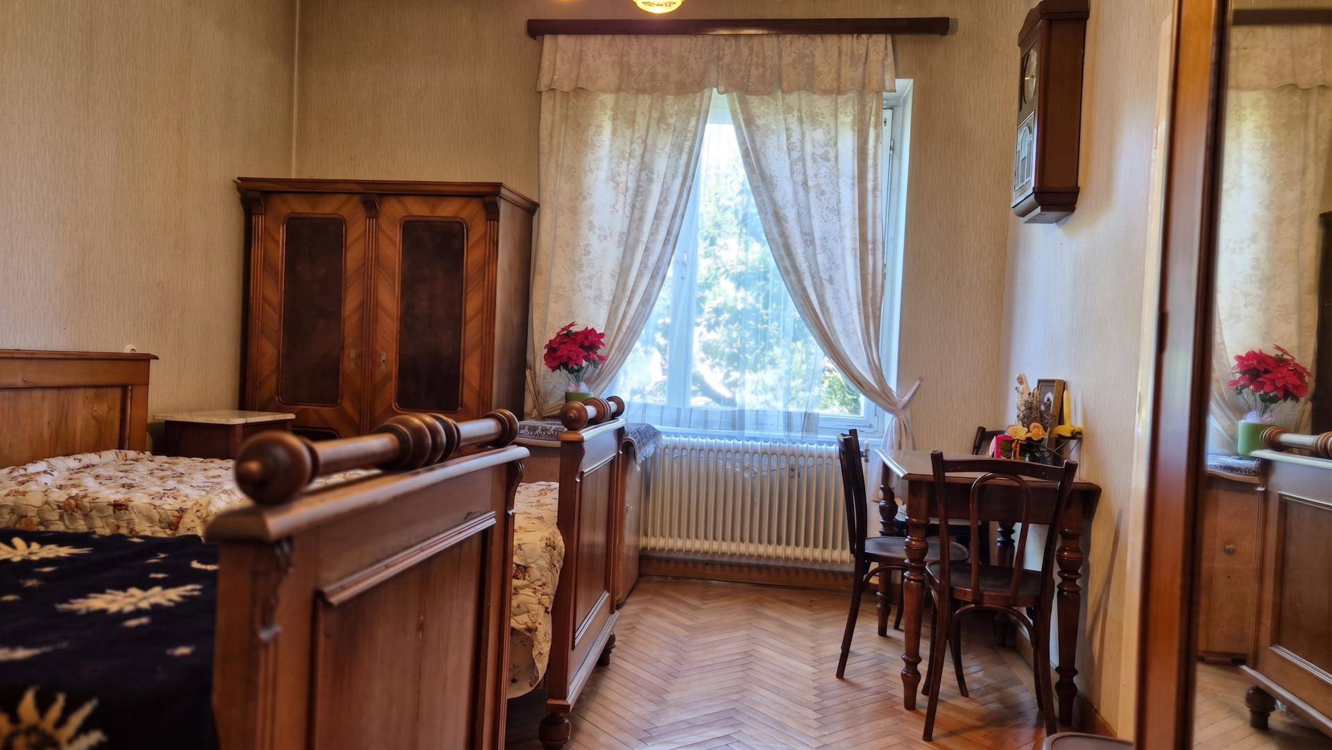 Schlafzimmer mit traditionellen Holzmöbeln, Parkettboden und einem Fenster mit Blick ins Grüne.