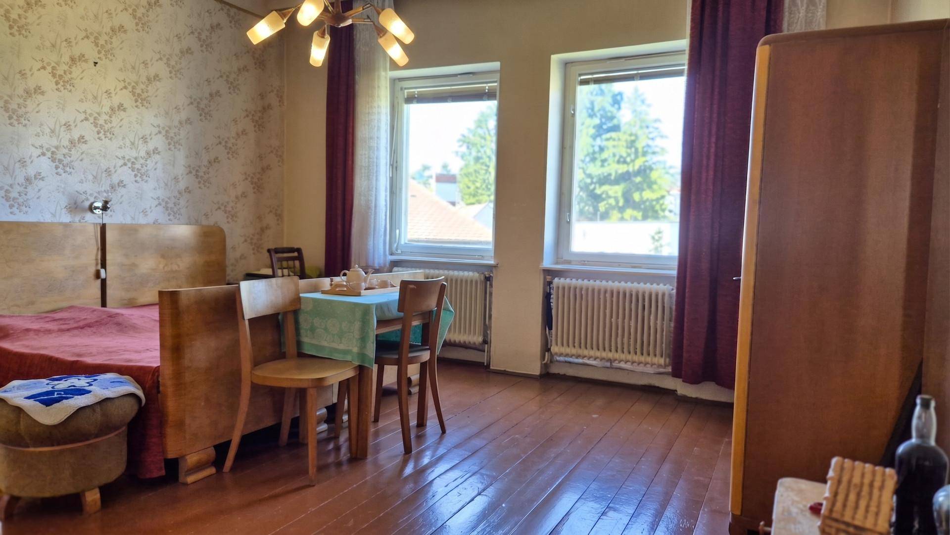Schlafzimmer mit Holzboden, zwei Fenstern und einem kleinen Tisch, eingerichtet im traditionellen Stil.