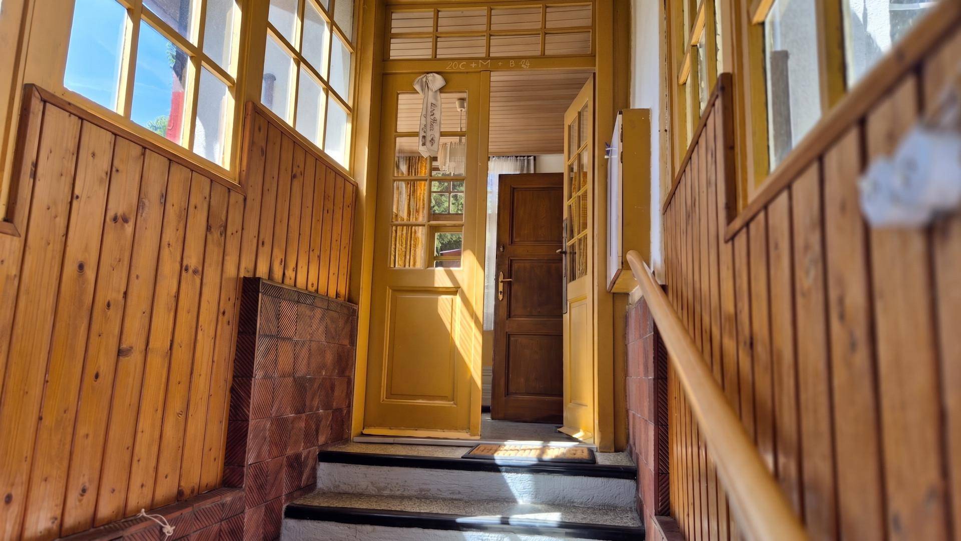 Heller Eingangsbereich mit Holzvertäfelung, gefliestem Boden und einer Treppe, die zum Haus führt.