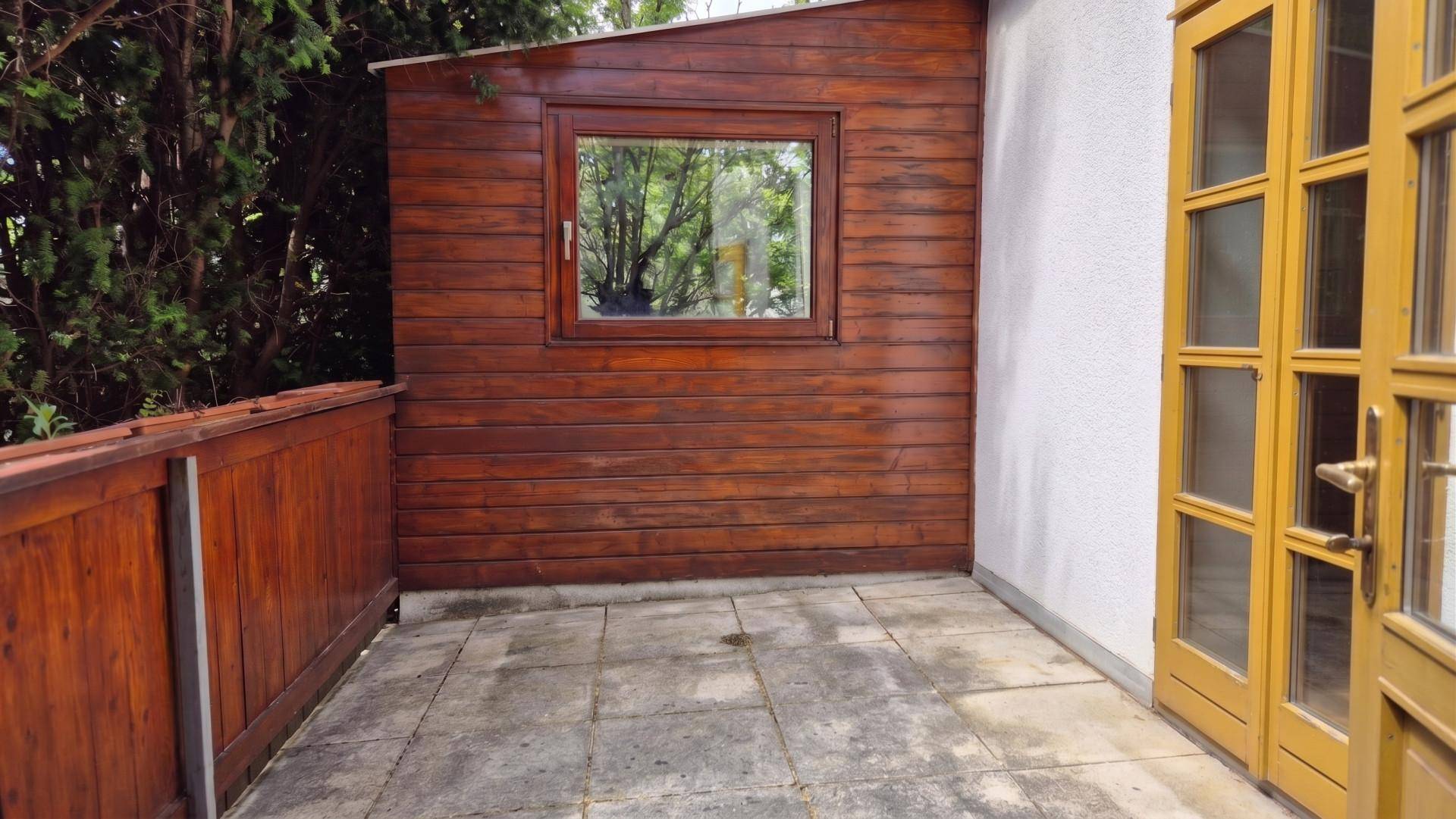 Kleine gepflasterte Terrasse mit Holzverkleidung und Zugang zum Gartenbereich.