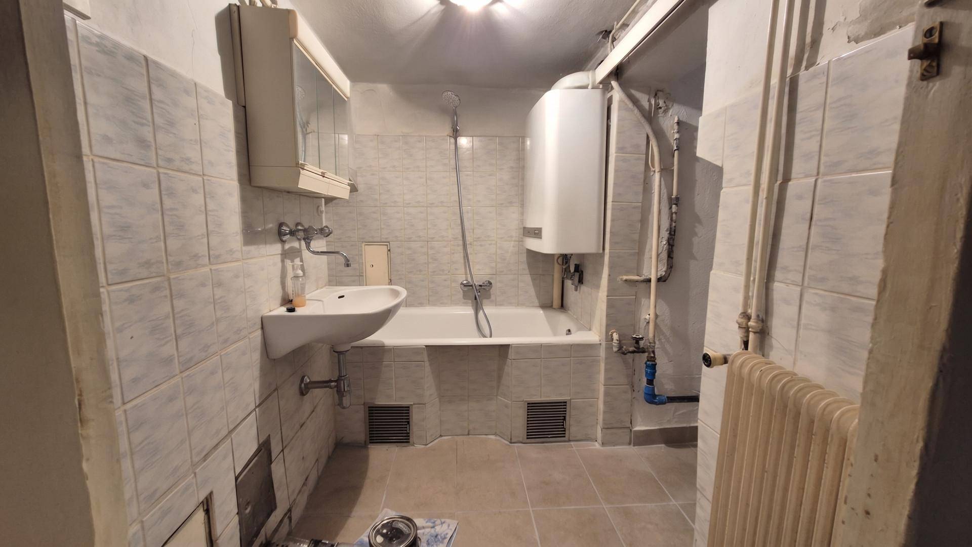 Einfaches Badezimmer im Keller mit Badewanne, Dusche und Fliesen im Retro-Stil.