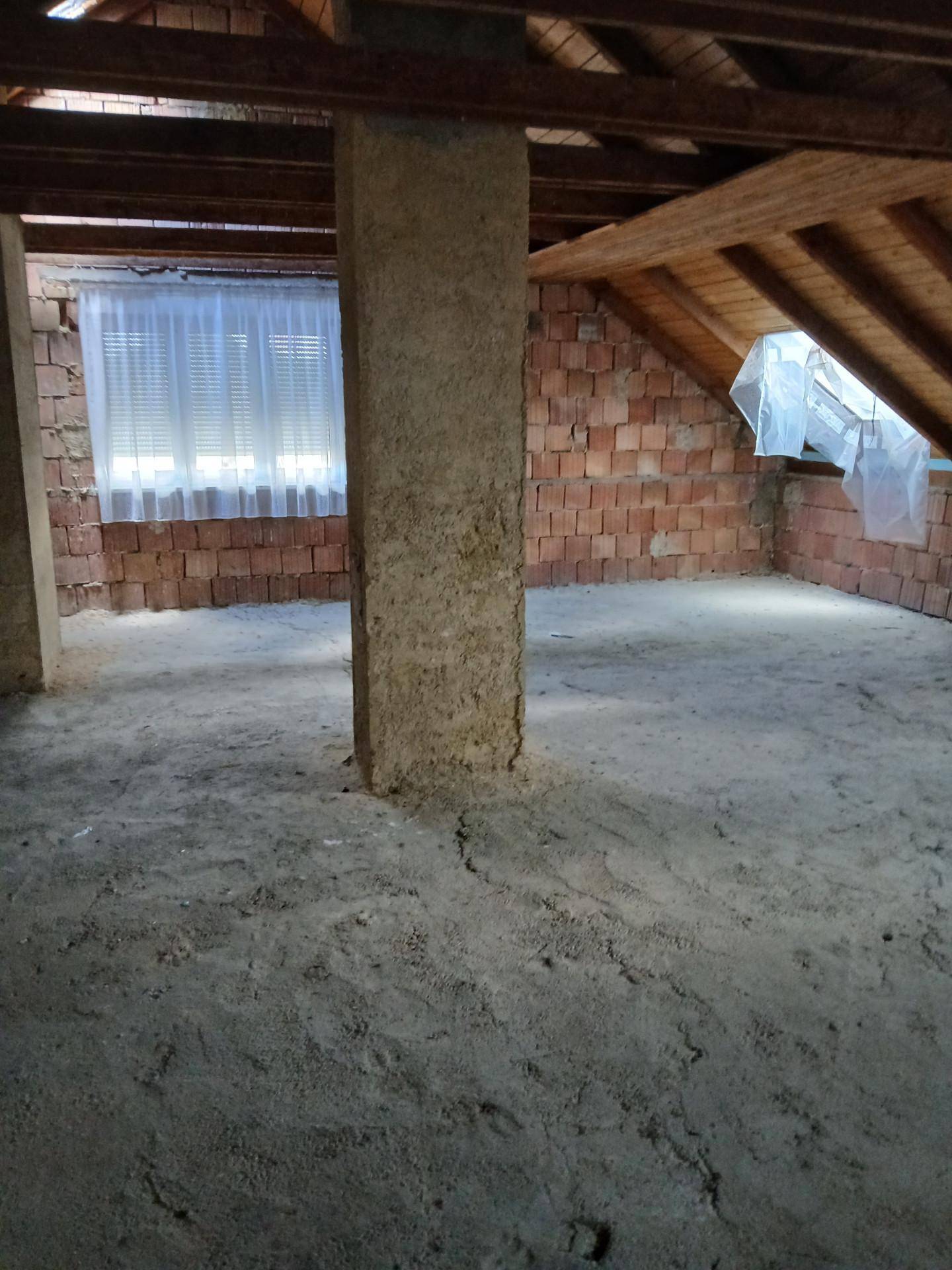 Unausgebauter Dachboden mit sichtbaren Holzbalken, Ziegelwänden und Betonboden, bereit für den Ausbau.