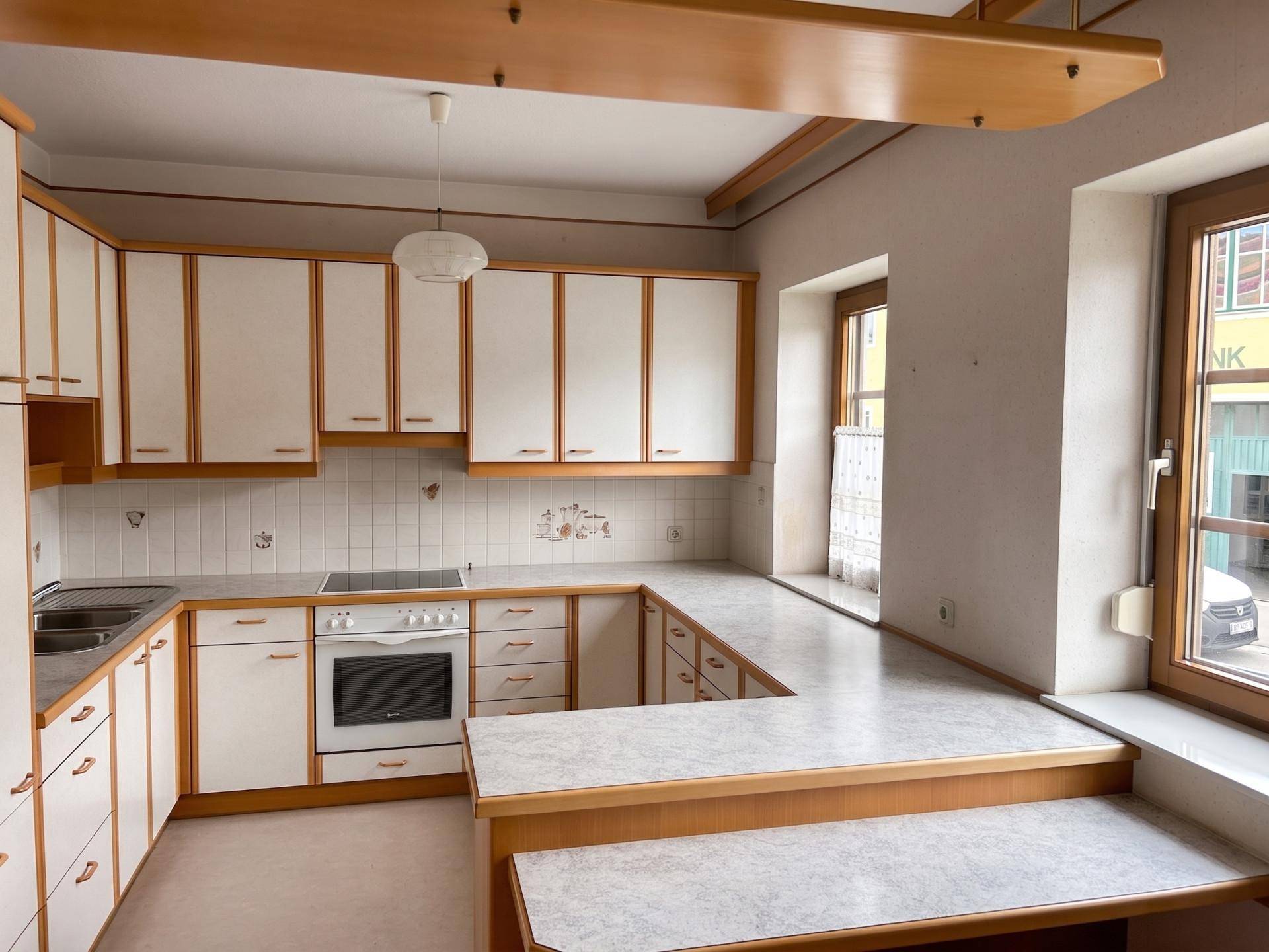 Helle Küche mit U-förmiger Arbeitsplatte, weißen Schränken und Holzdetails, ideal für den täglichen Gebrauch.