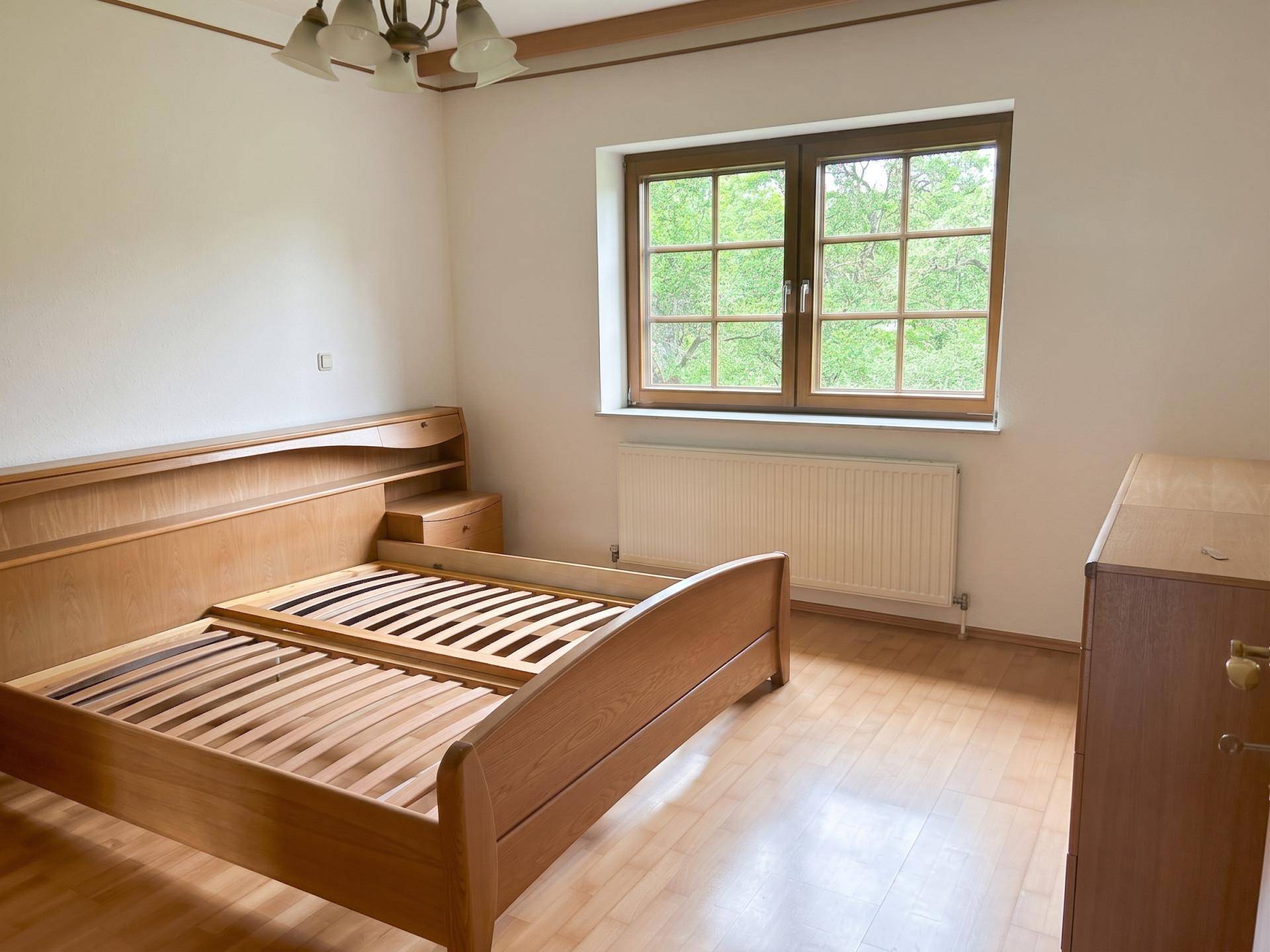 Schlafzimmer mit Holzbett und Parkettboden, bietet einen ruhigen Rückzugsort mit Blick ins Grüne.