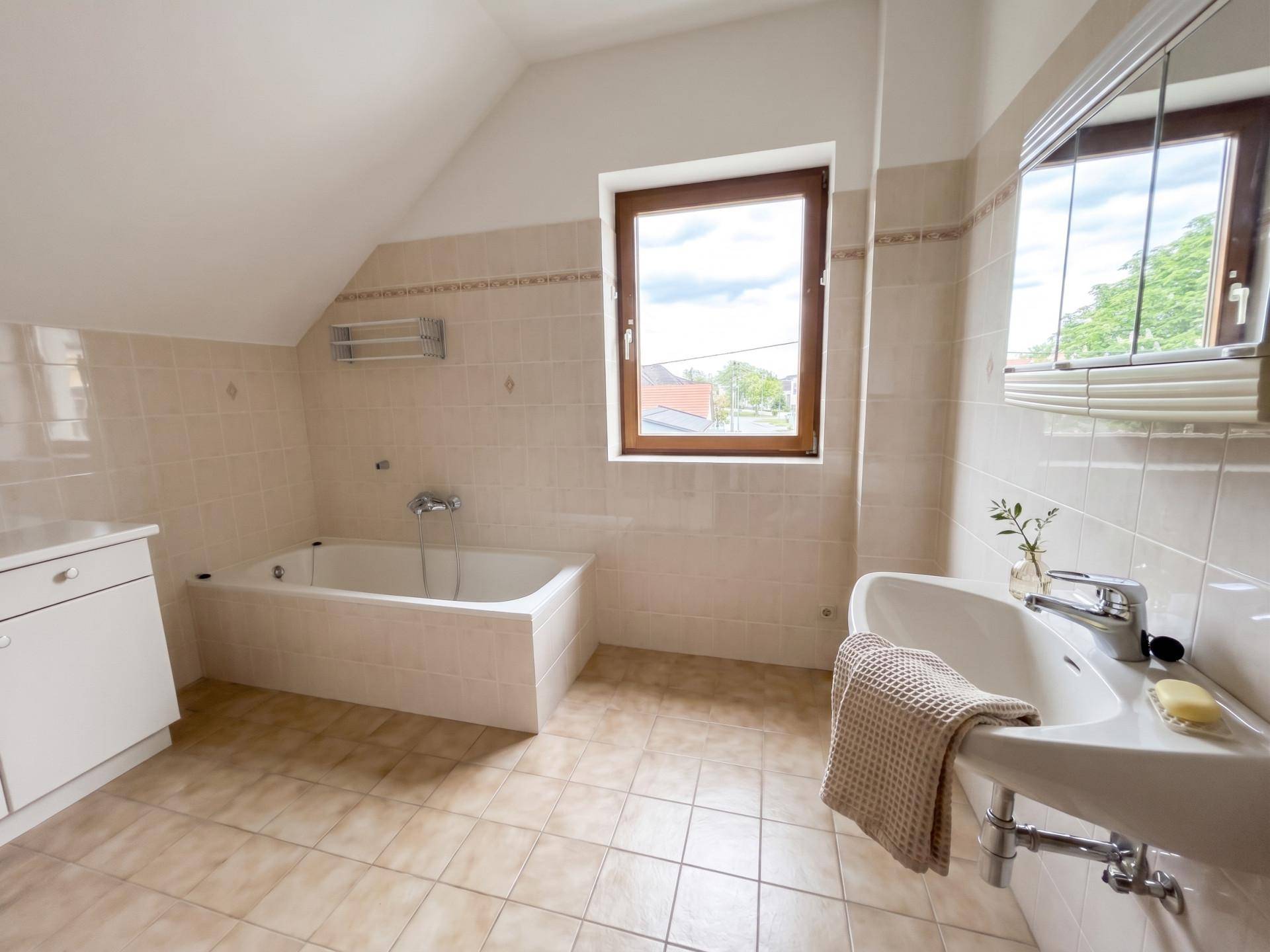 Geräumiges Badezimmer mit Badewanne, Waschbecken und Fenster, bietet viel Tageslicht.