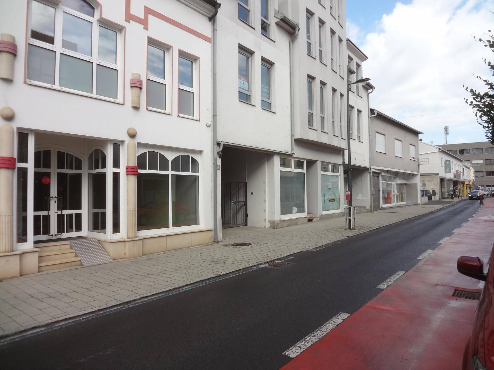Straßenansicht mit verschiedenen Gebäudefassaden und einem roten Fahrradweg im Vordergrund unter bewölktem Himmel.