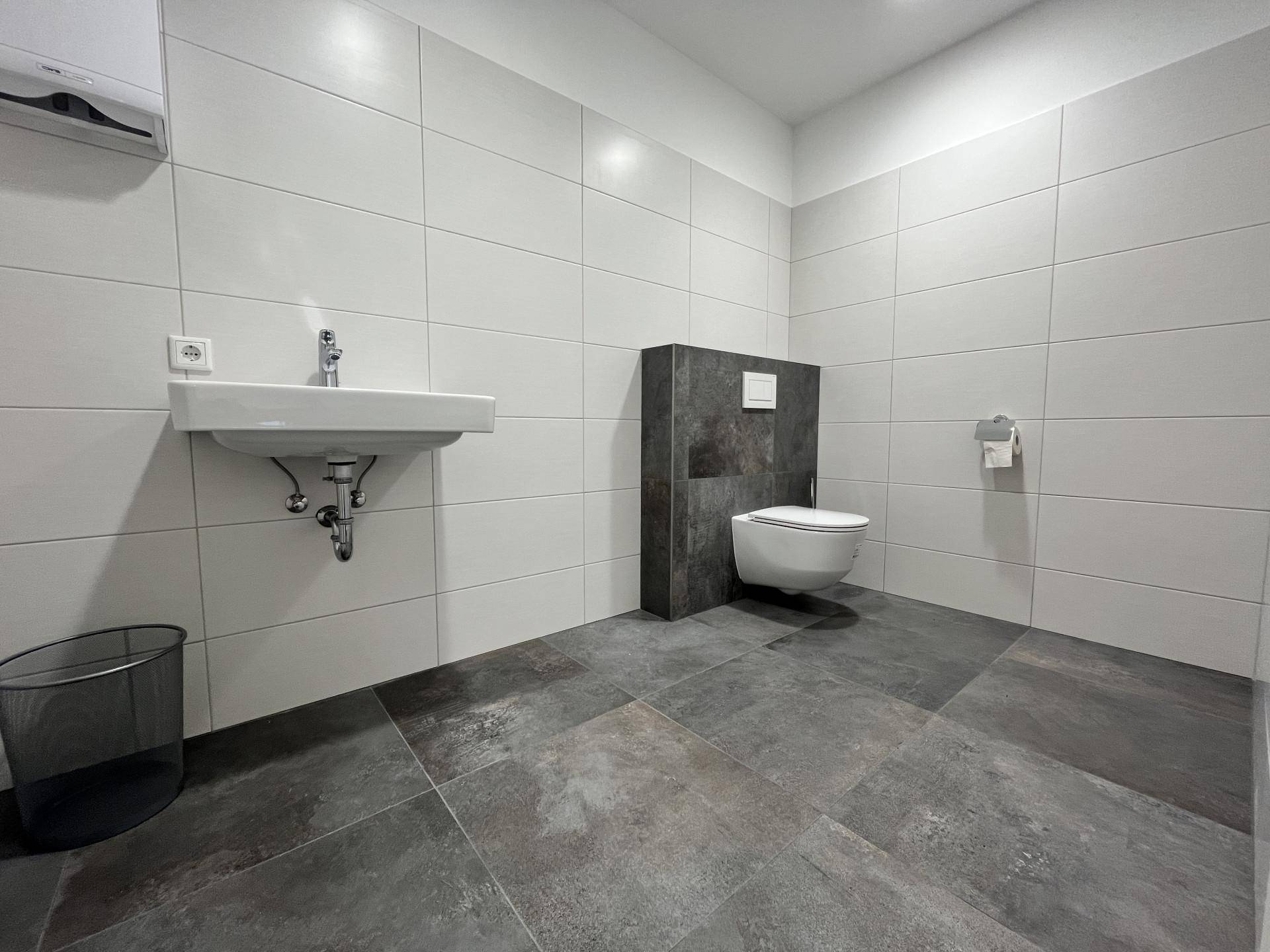 Modernes Badezimmer mit weißen Wandfliesen und dunklen Bodenfliesen, ausgestattet mit Wand-WC und Waschbecken.