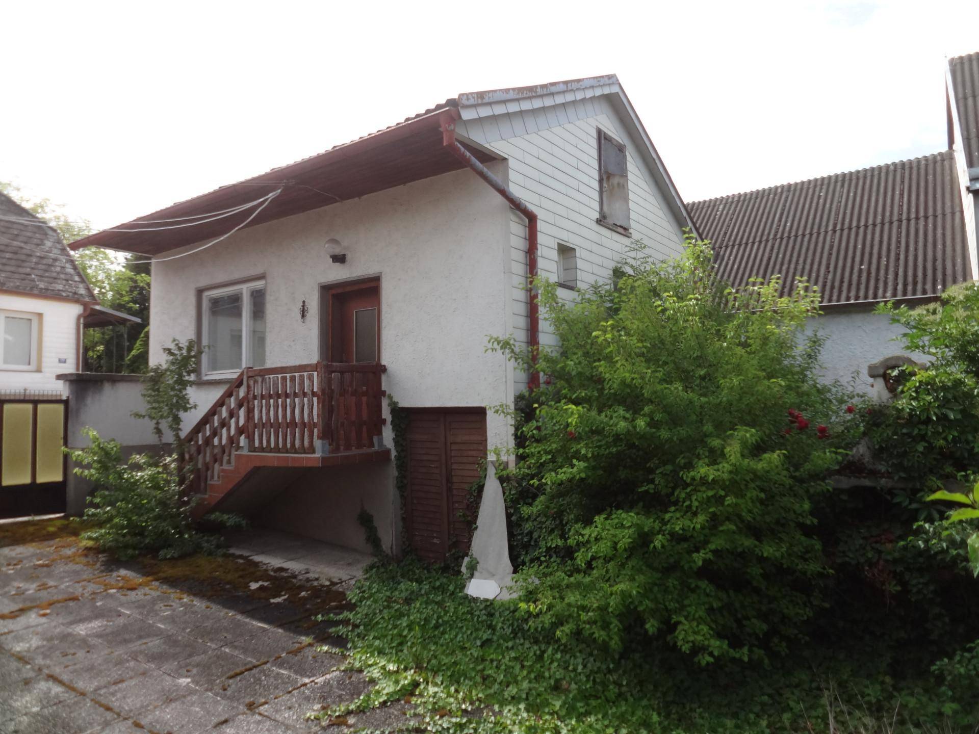 Rückseite des Hauses mit Außentreppe, Holzbalkon und stark bewachsenem Gartenbereich.
