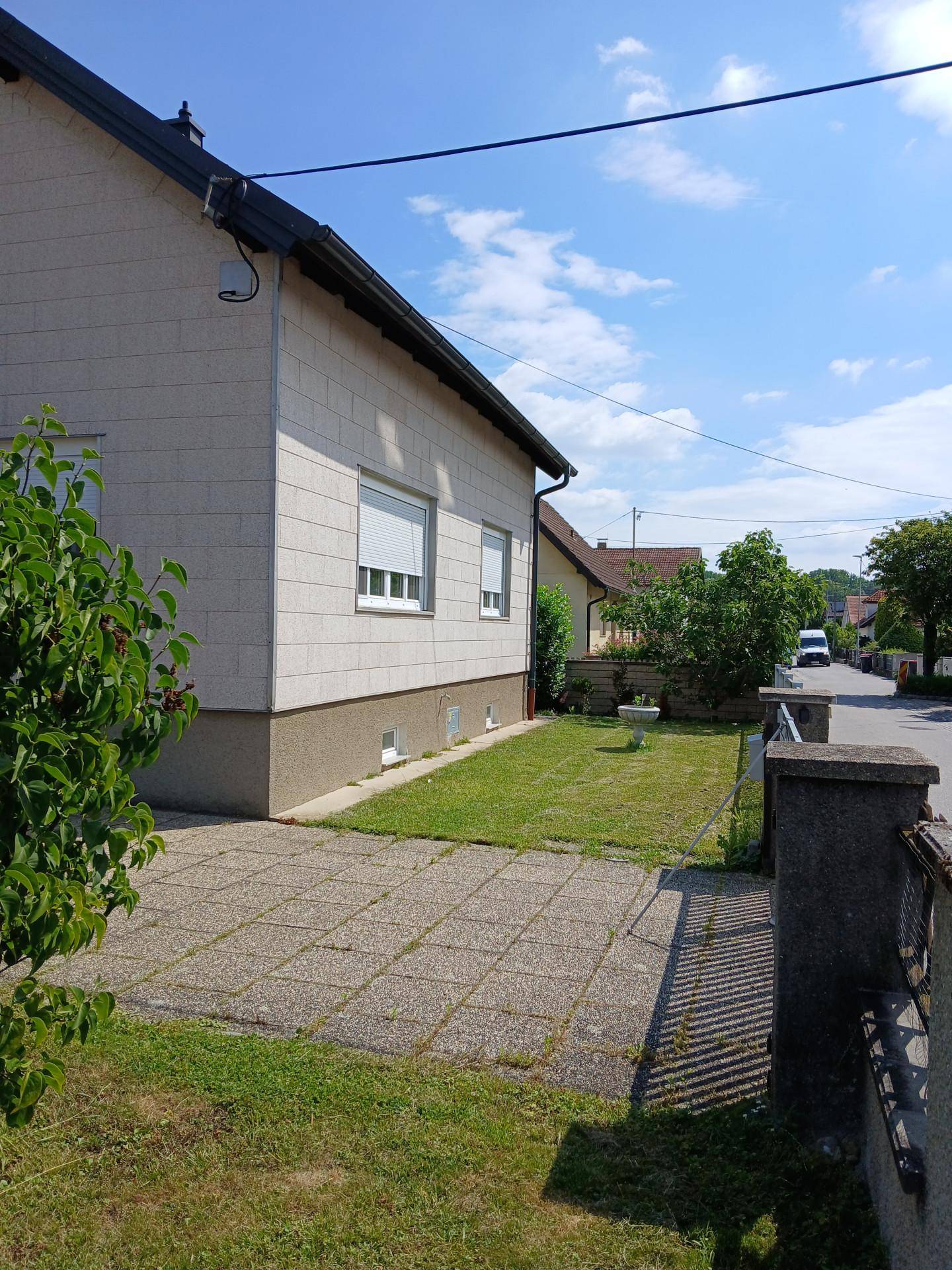 Seitenansicht des Hauses mit gepflastertem Bereich, Rasenstreifen und Blick auf die Straße.
