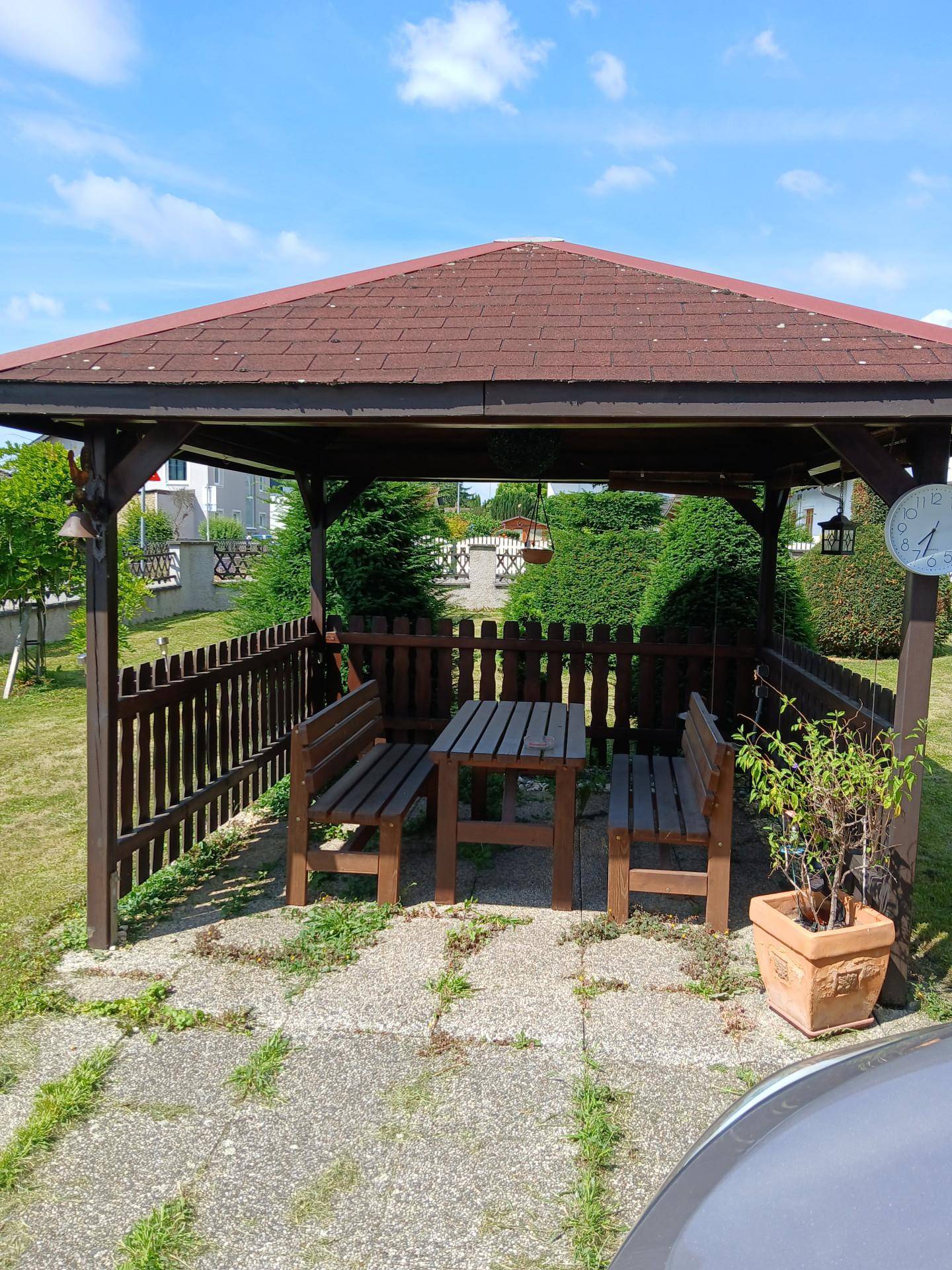 Gemütlicher Holzpavillon im Garten mit Tisch und Bänken, ideal für Mahlzeiten im Freien.