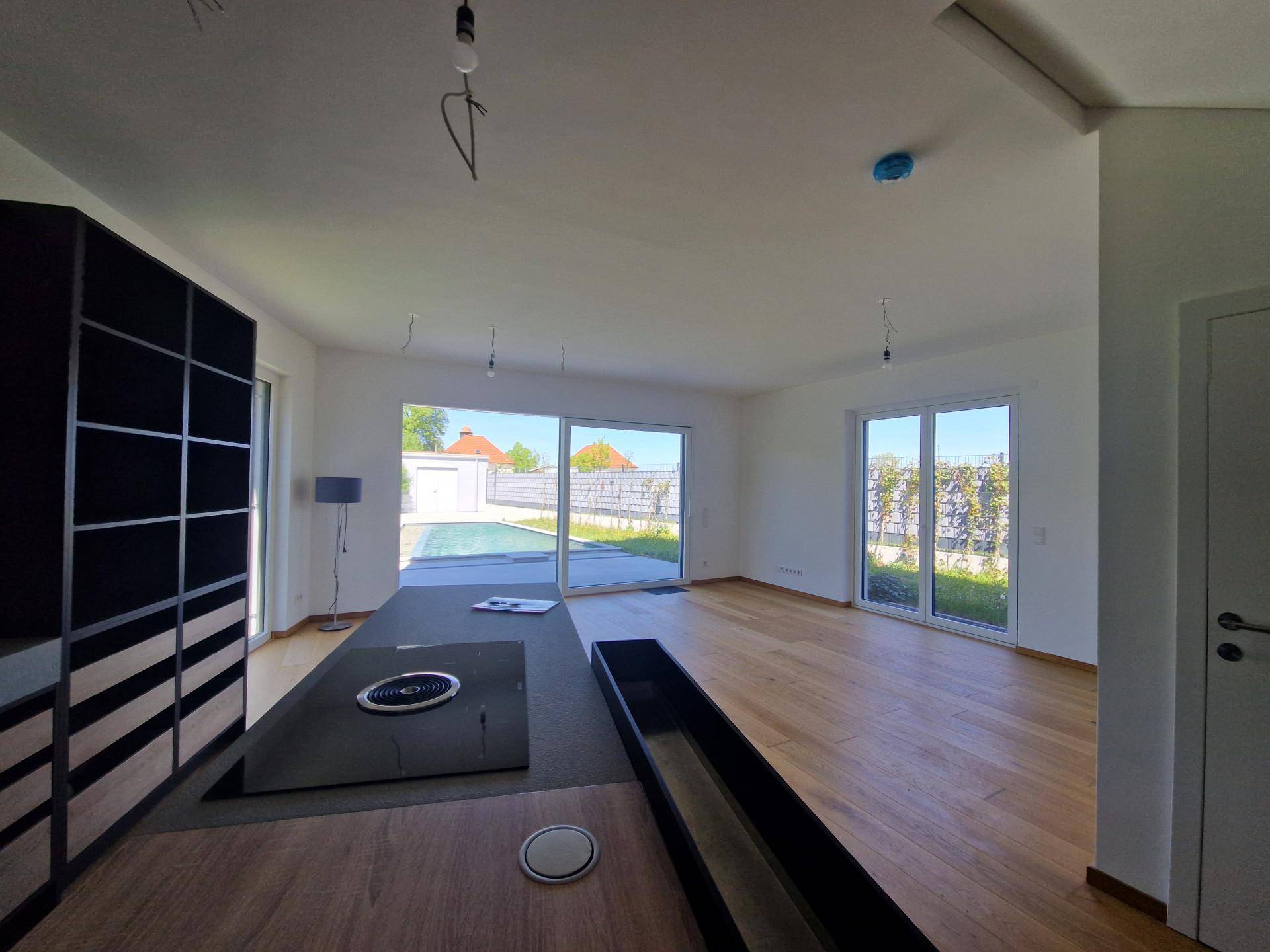 Moderne Küche mit Kochinsel und Induktionskochfeld, großen Fenstern und Blick auf den Poolbereich.